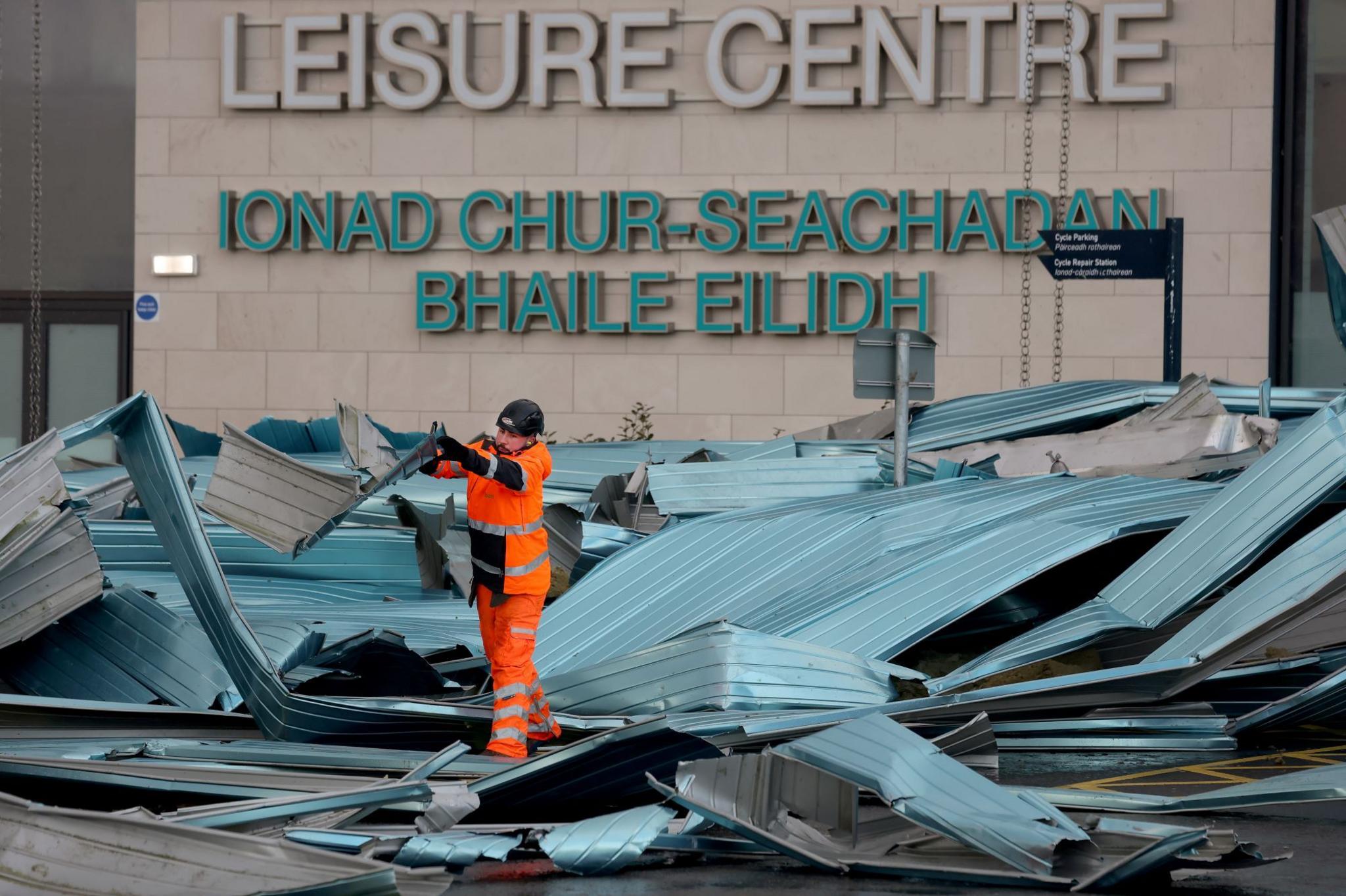 A worker in orange reflective work clothing throwing damaged pieces of a blue/grey plastic roof outside the Helensburgh Leisure Centre