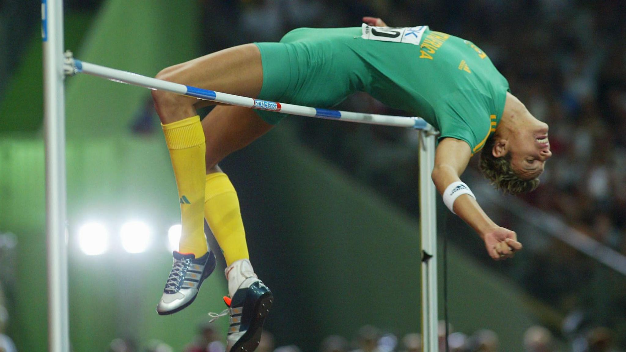 Jacques Freitag wears and green South Africa athletics kit as he bends his back while narrowly clearing the bar competing in the high jump