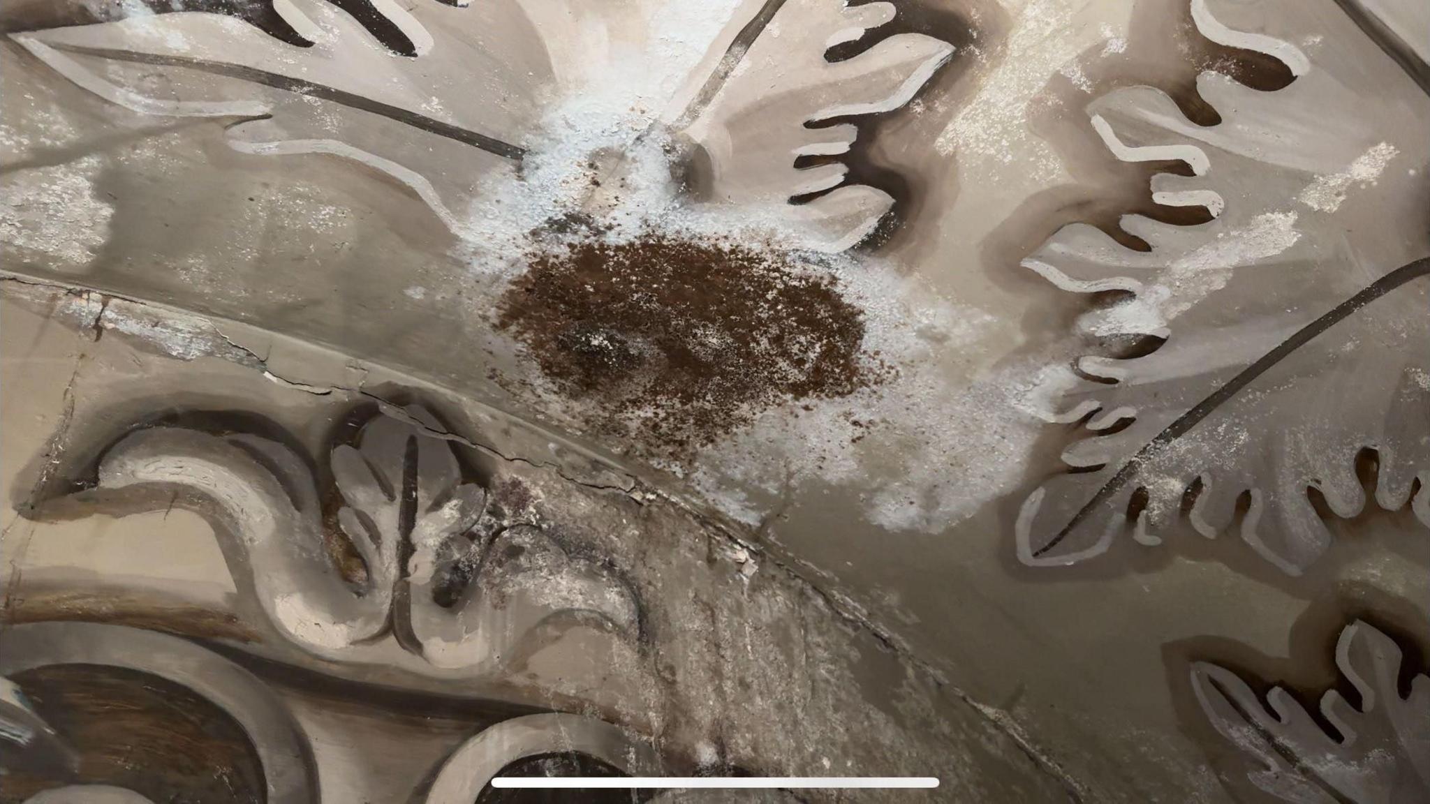 A large circular white and brown water damage stain is visible covering decorative stonework with flower shapes. Large white drip stains can be seen underneath.