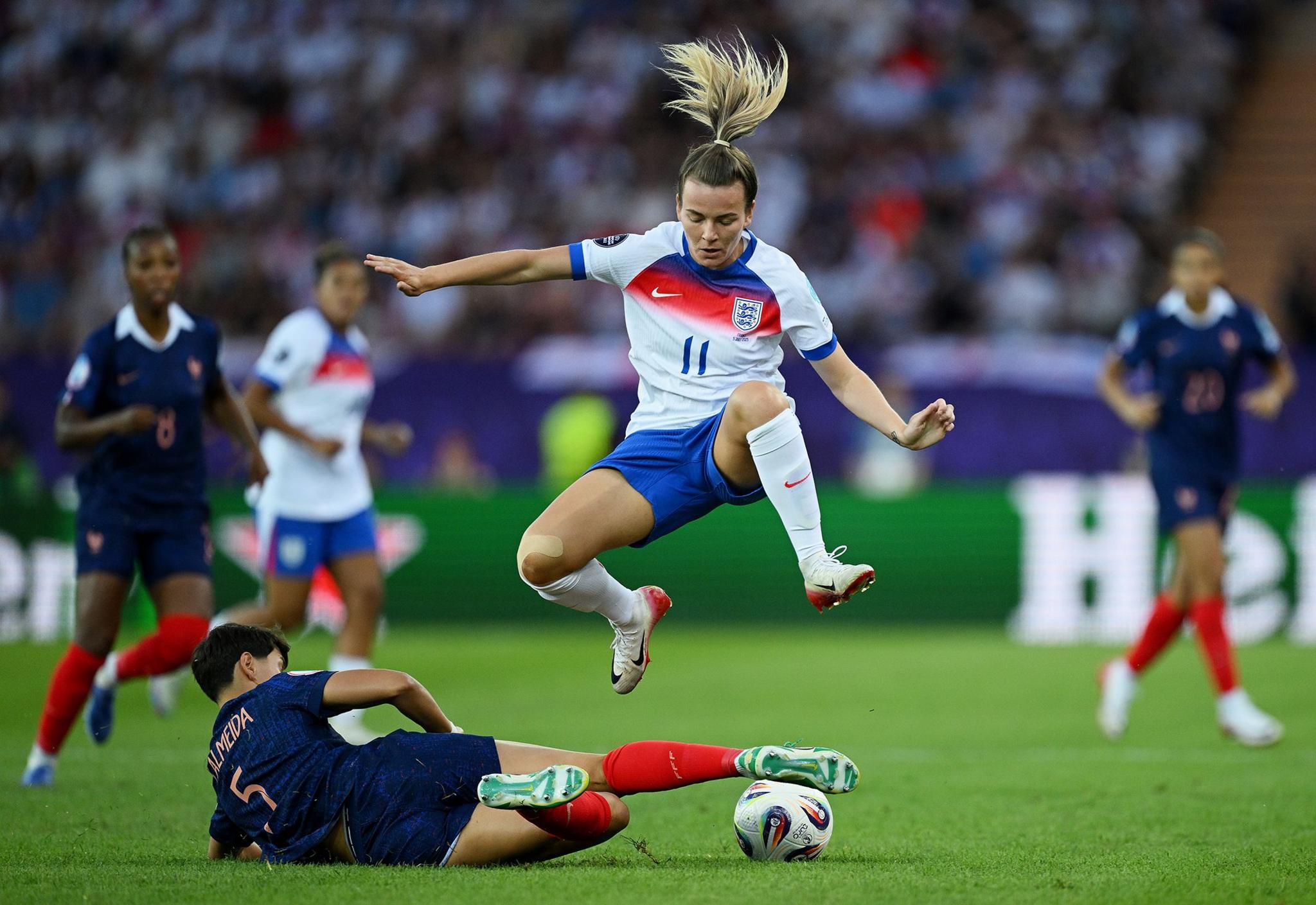 England's Lauren Hemp leaps over a sliding tackle from France's Elisa De Almeida. Photo by Matthias Hangst