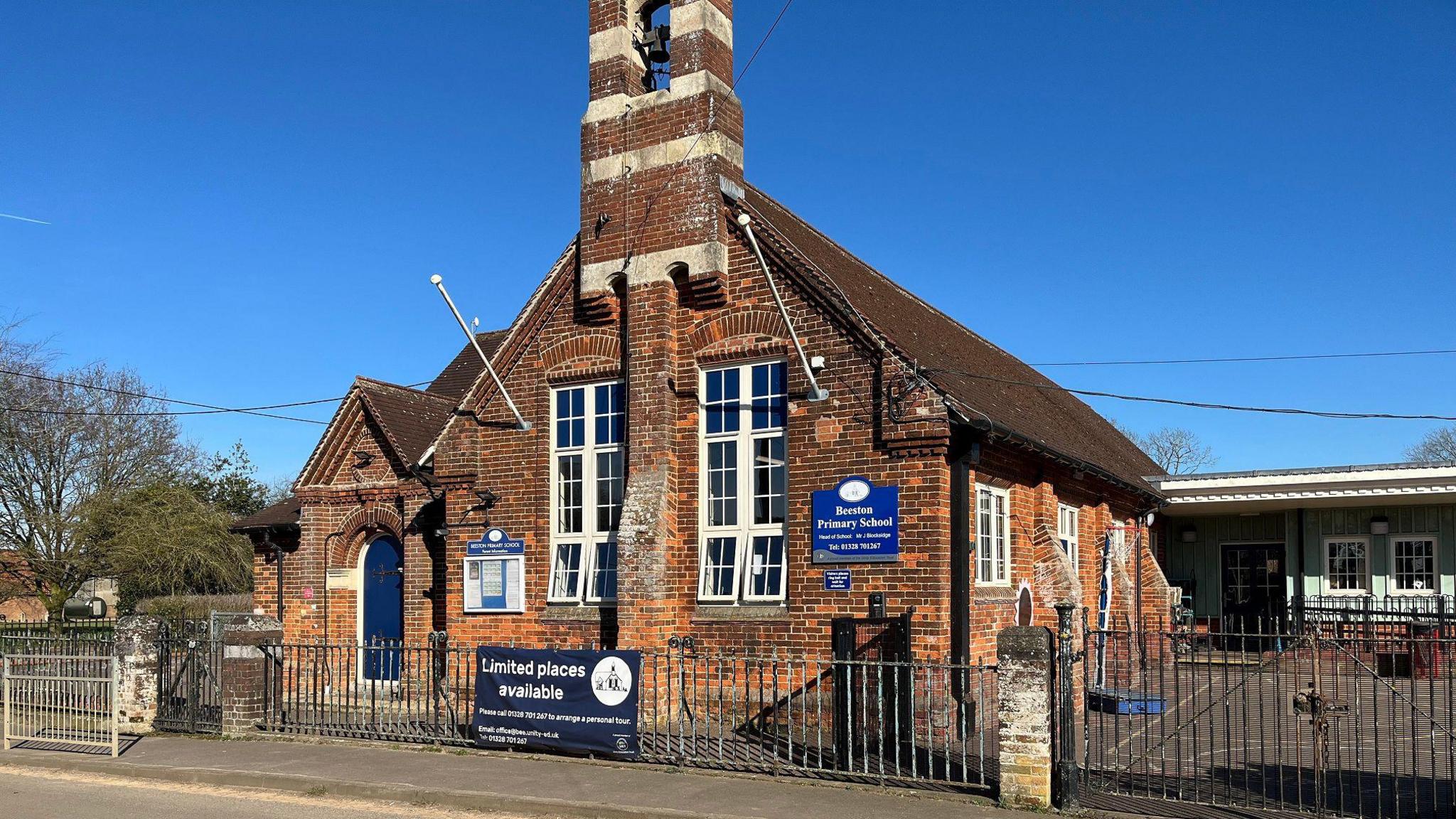 Beeston Primary School is an old fashioned brick building with a bell tower. There is a blue sign saying the name of the school and a banner proclaiming "limited places available". 