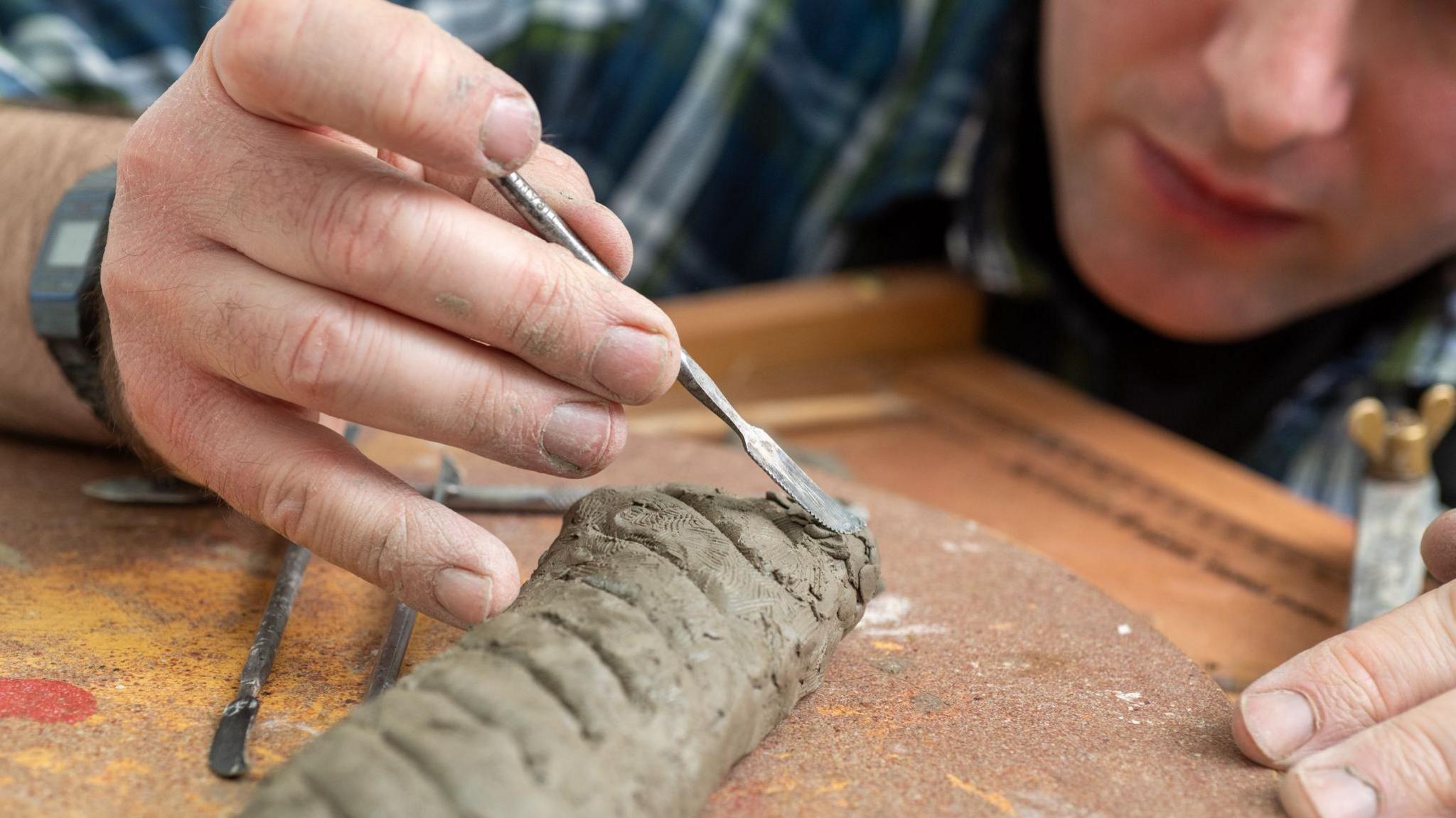 The wax sausage roll in the making, a man pats the unfinished sculpture with a tool