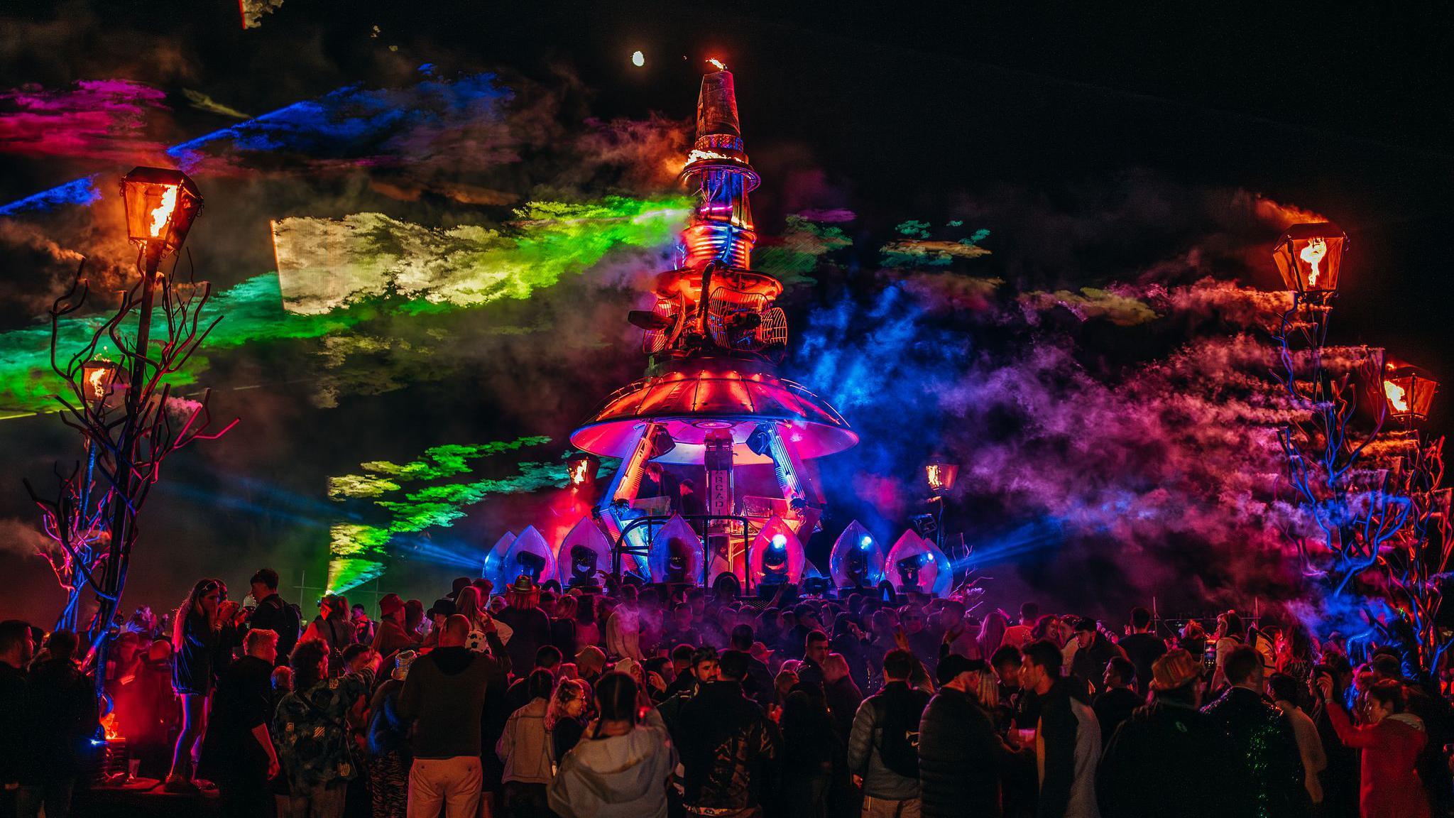 A tall neon structure surrounded by people at night as it lights up the sky