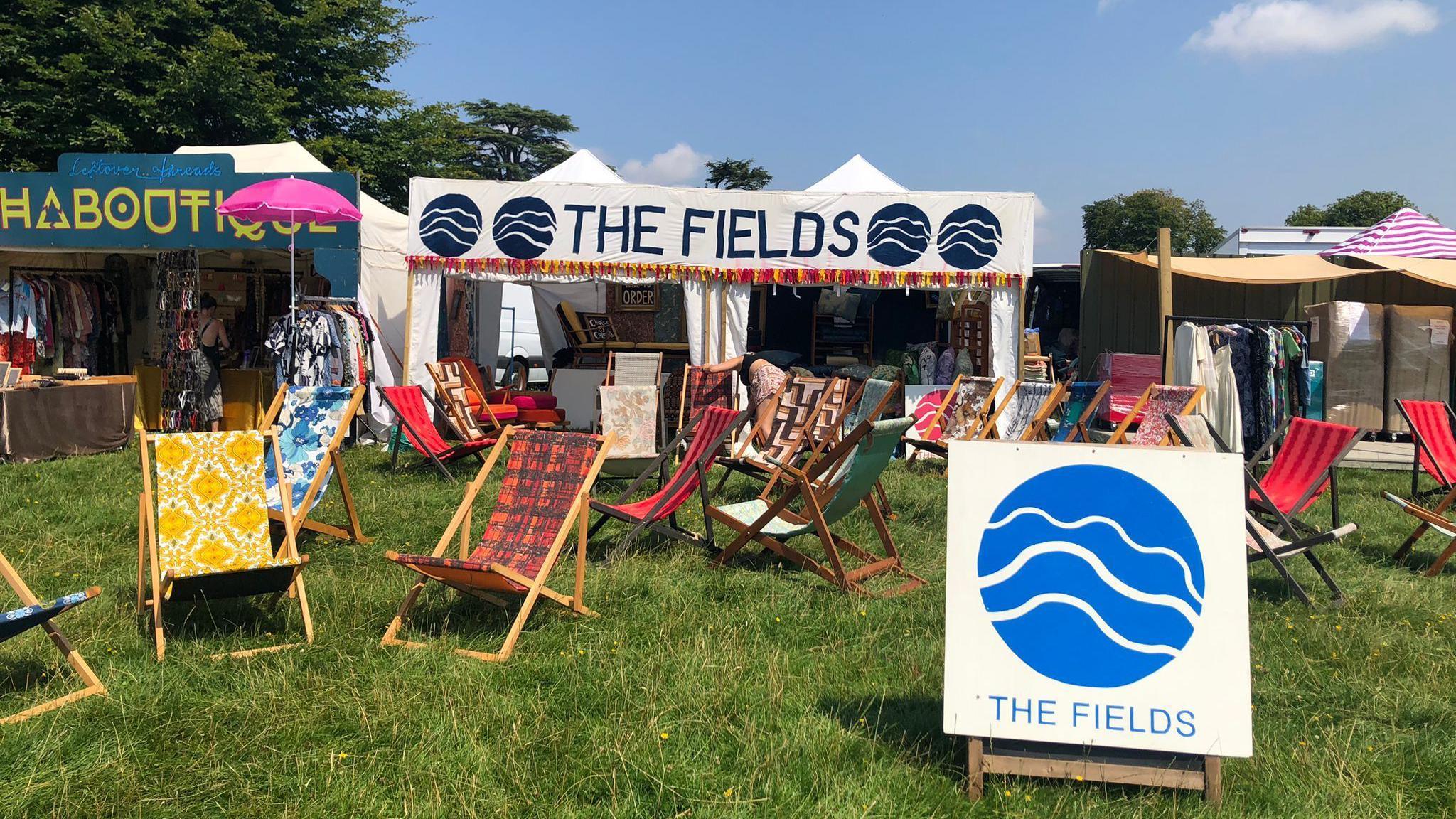 The Fields stall set up with deck chairs dotted on the grass in front of the main white stall with 'The Fields' printed at the top.