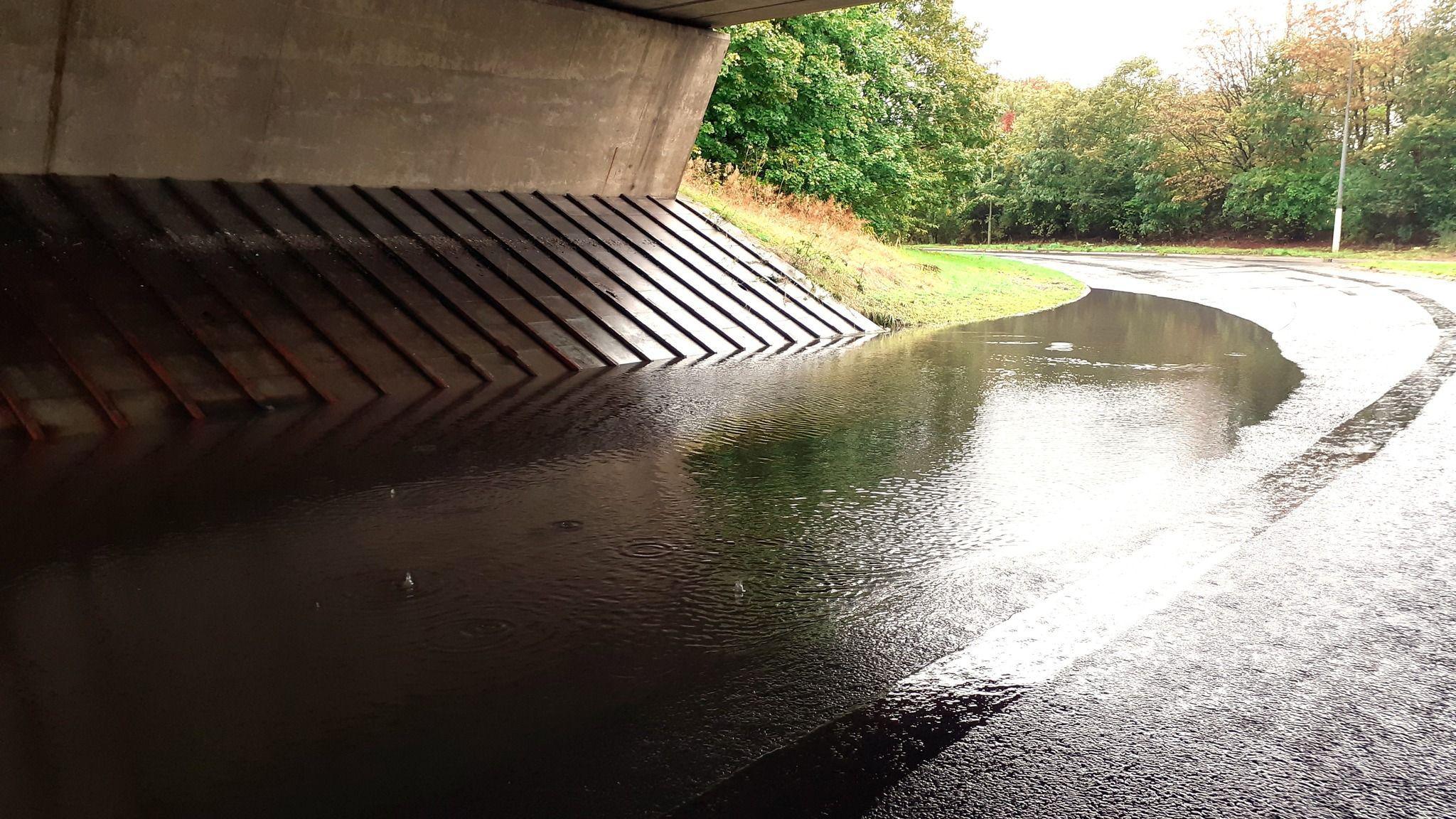 A flooded road that runs beneath a bridge. 