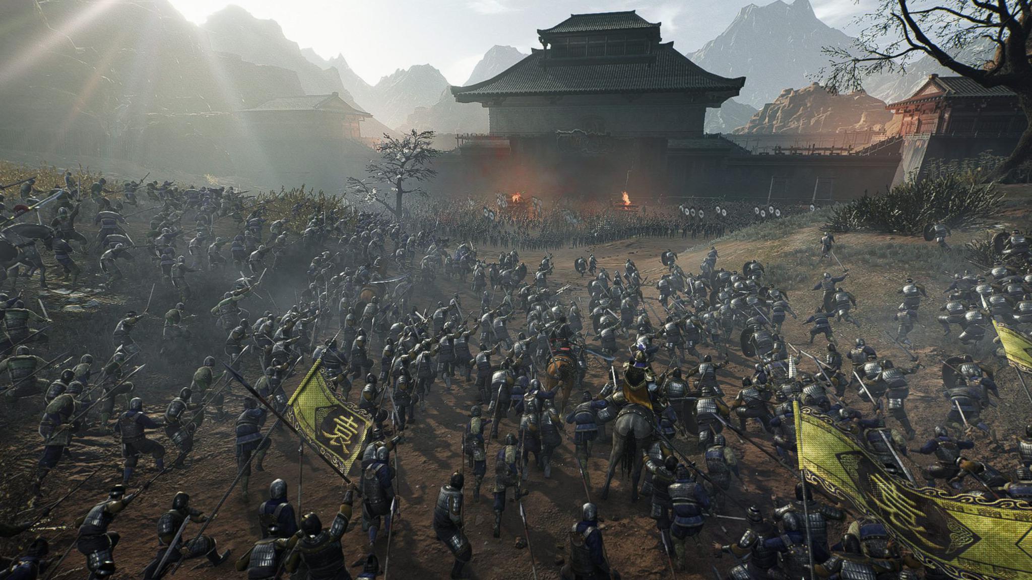 A battle sequence from the game. There are many hundreds of soldiers in feudal era armour running towards one another holding pikes, swords and other similar era-appropriate weapons. There is a Chinese temple in the background, with mountains behind.