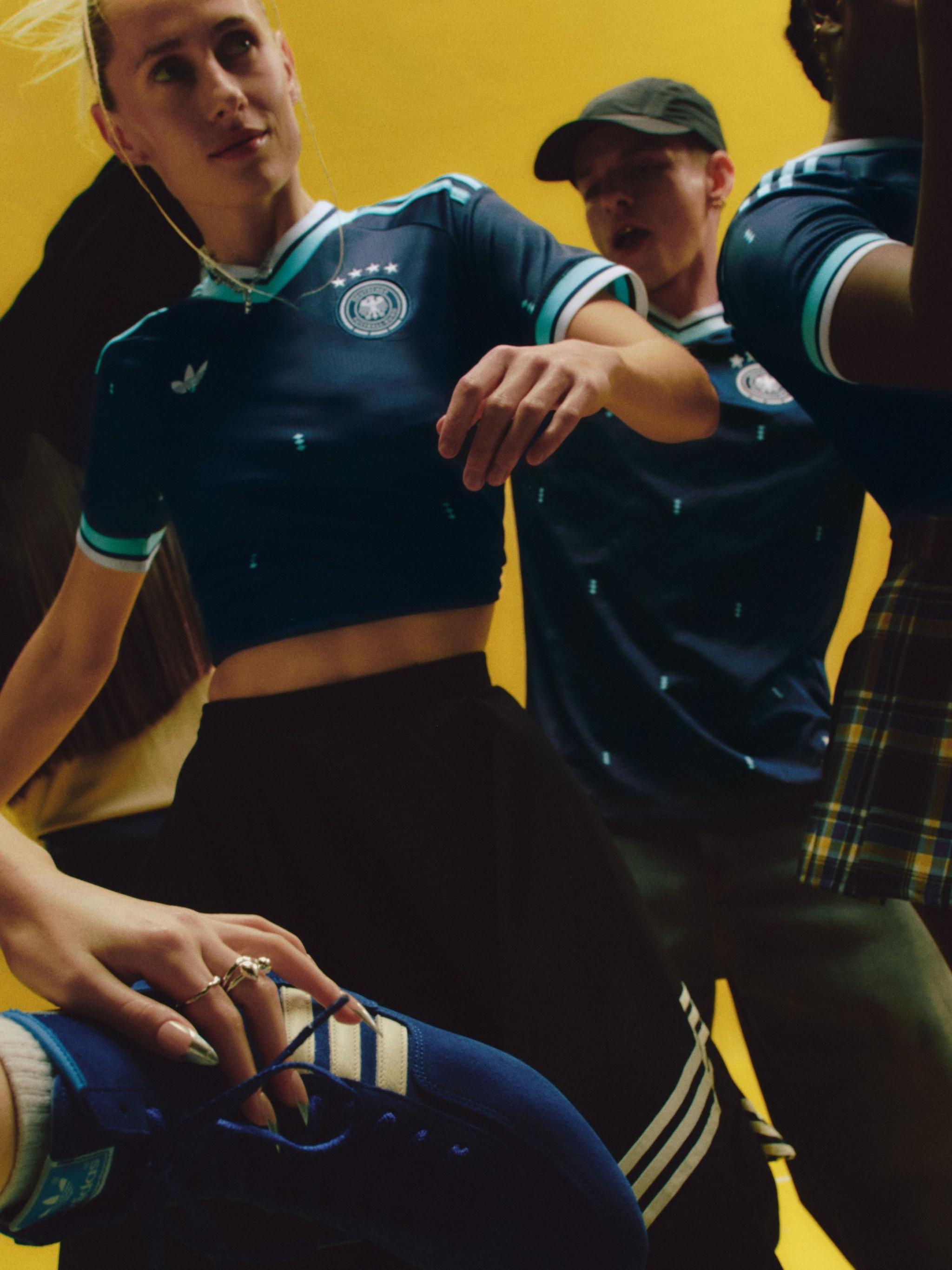 Foto e një gruaje me një uniformë të shkurtuar Adidas të Gjermanisë si mysafir, e veshur me atlete të zeza.