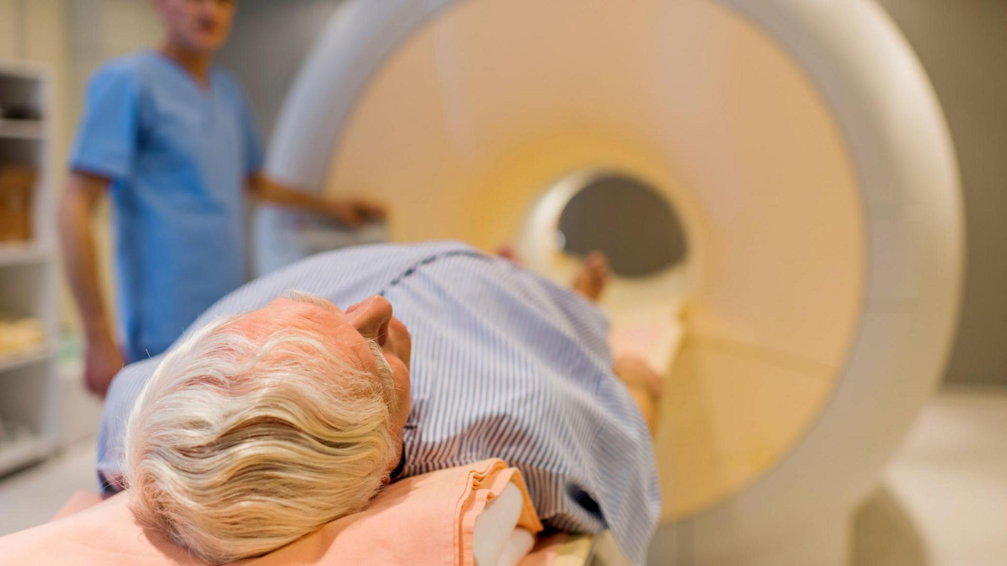 Man with grey hair lying down about to enter an MRI machine.