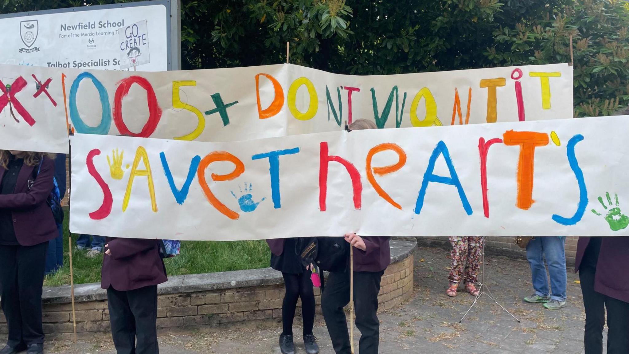 School children hold up a bright colourful banner which covers their face