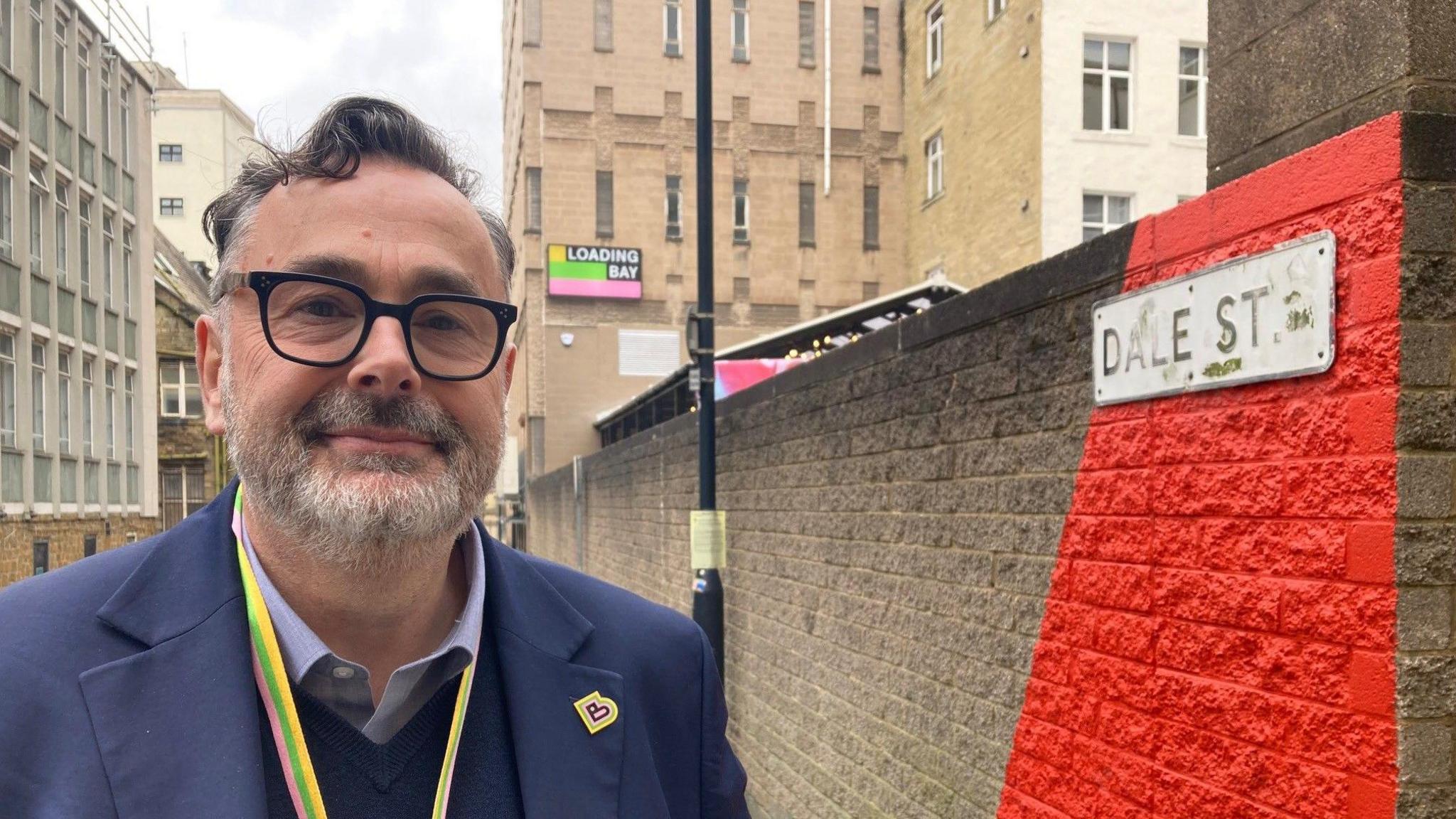 A man wearing glasses and blue jacket standing next to a wall painted with a bright red stripe