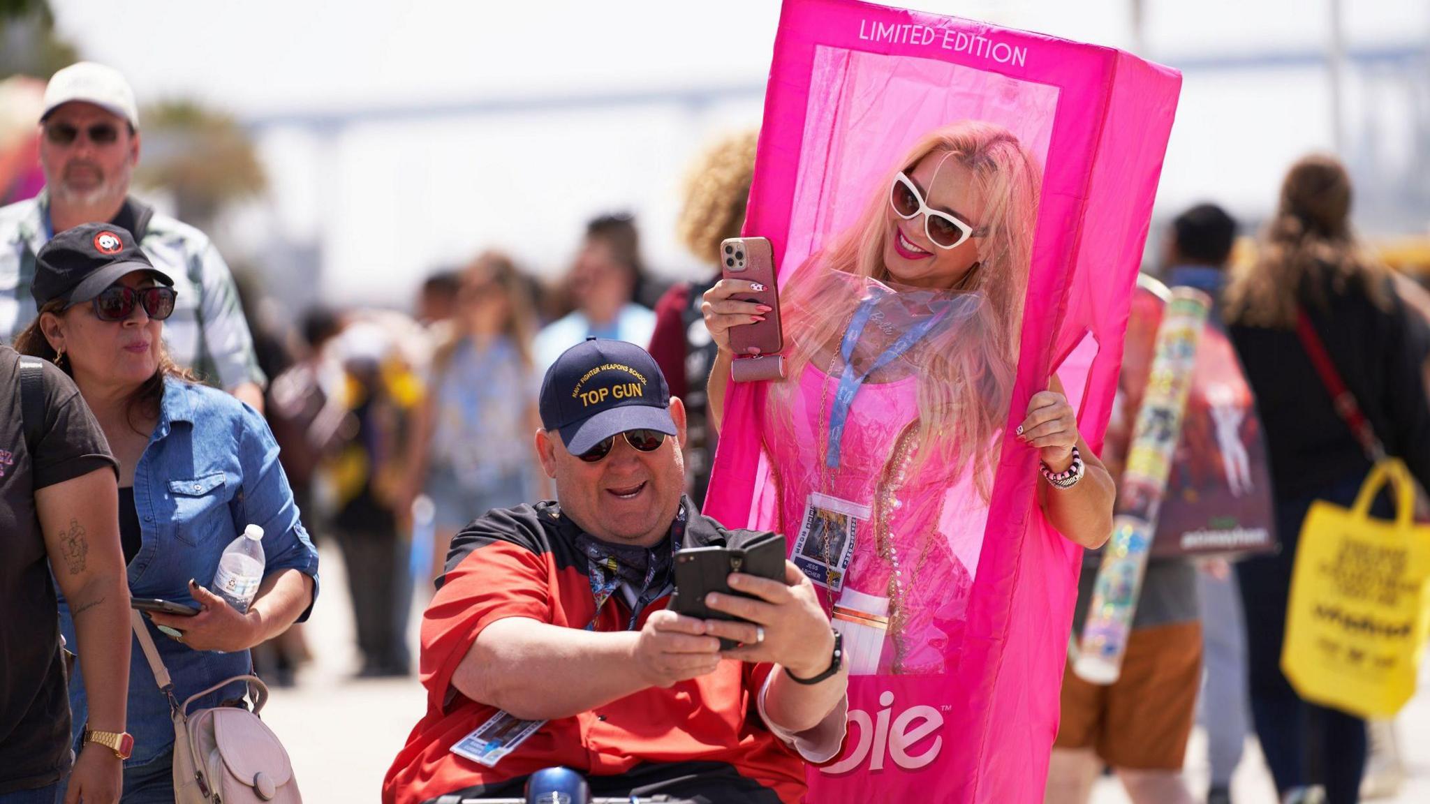 A lady in a Barbie costume getting a selfie with an older man in a wheelchair