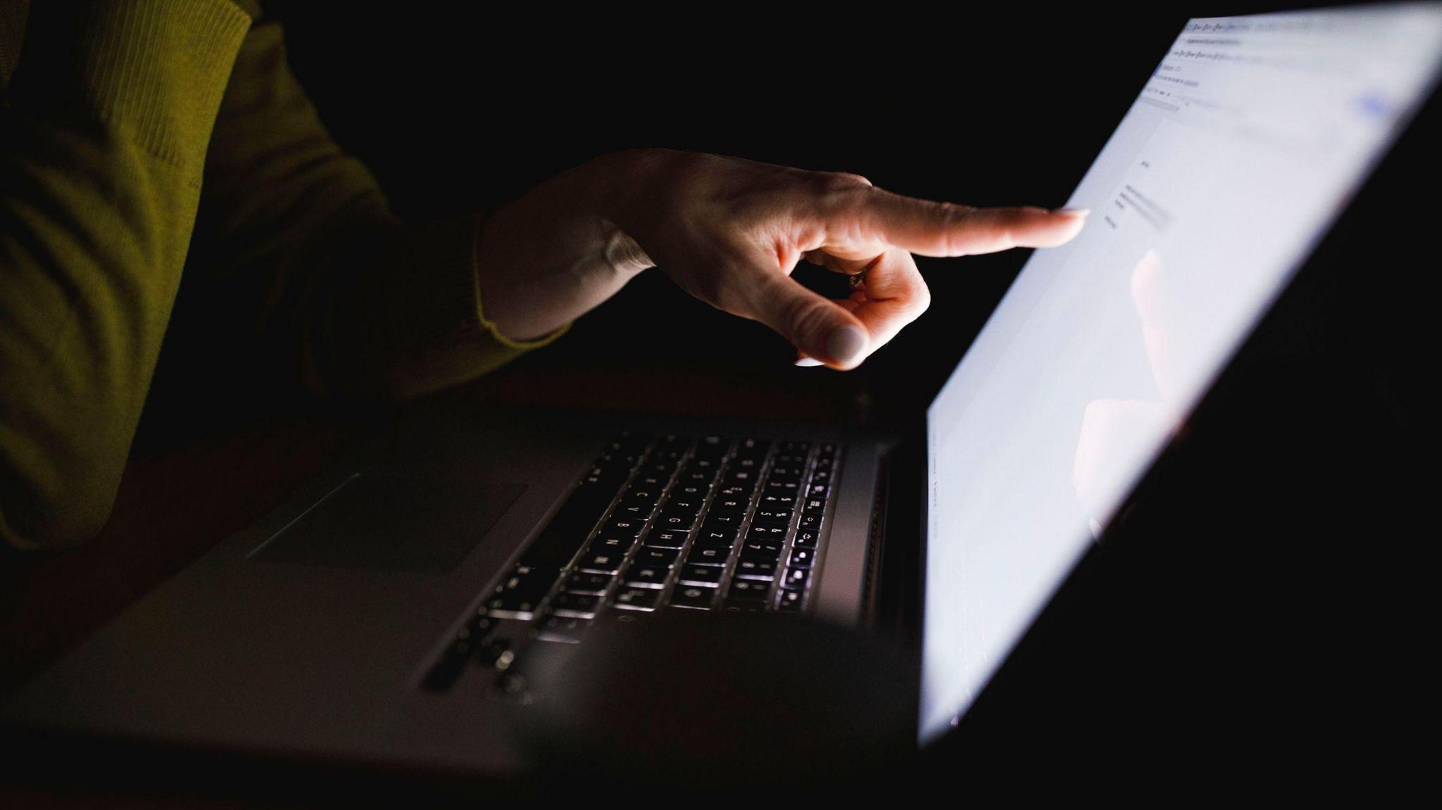 A dark room with a person pointing at a laptop.