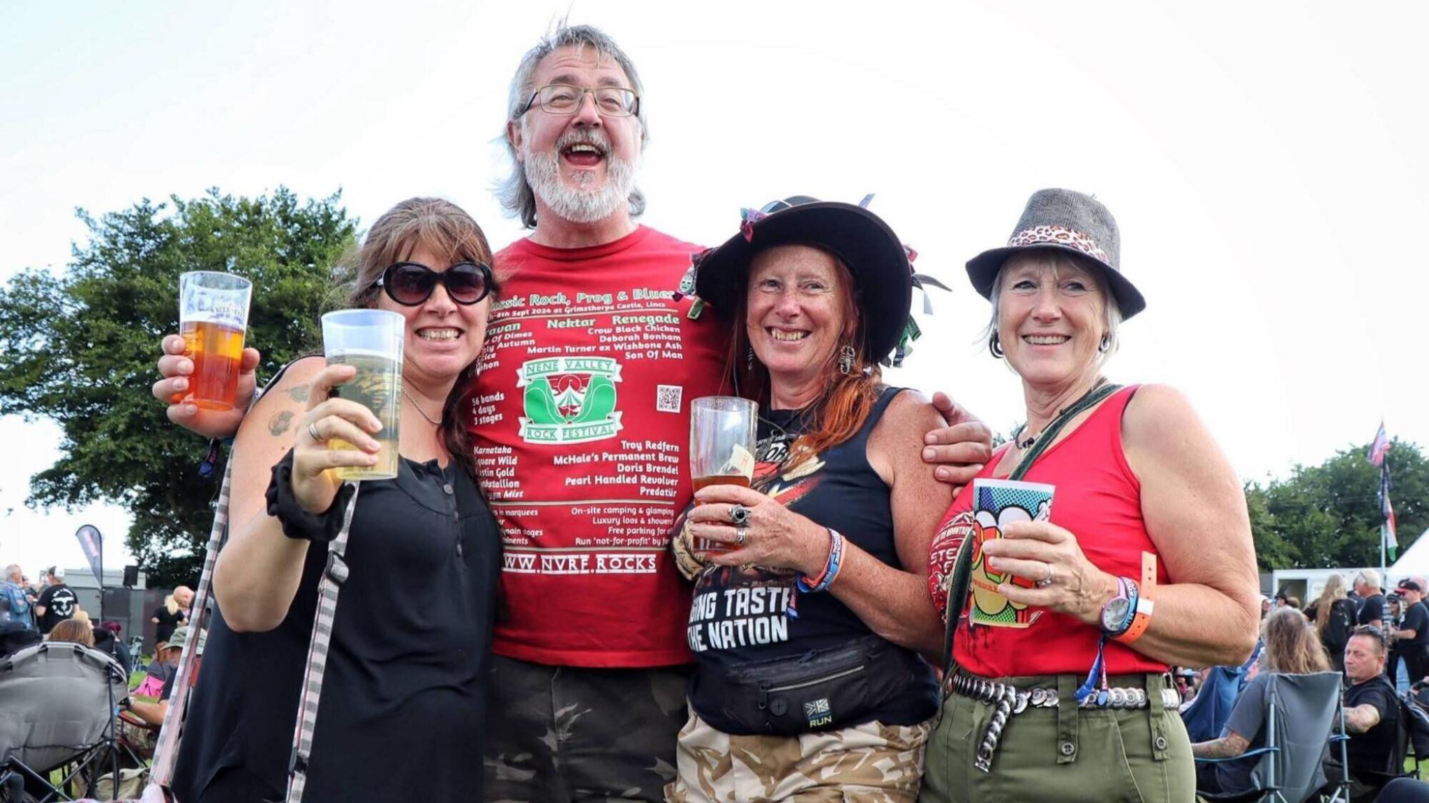 A man and three women at a rock festival, holding drinks.