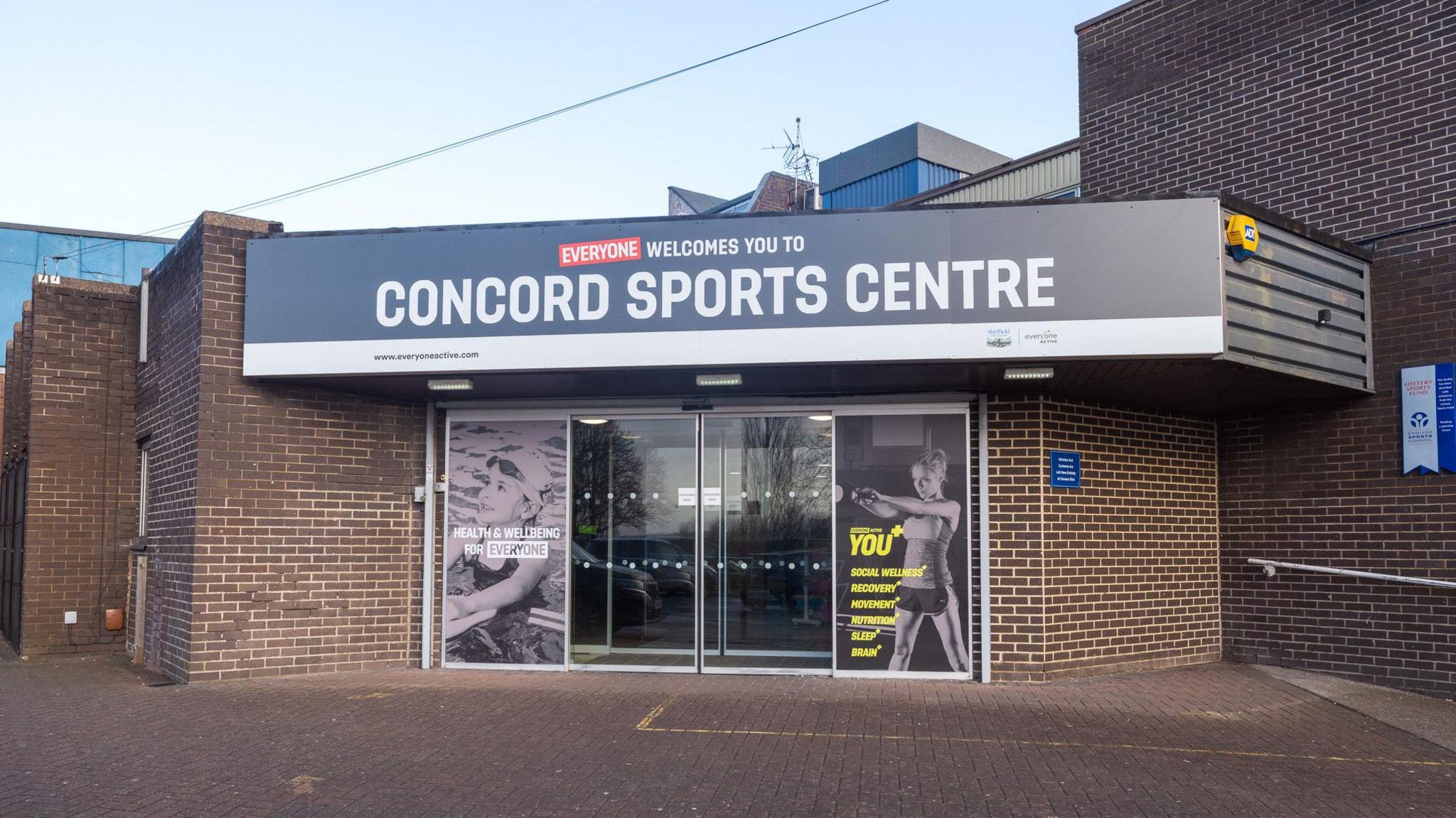 A sports centre entrance with sliding glass doors and photographs of children swimming and exercising at the gym