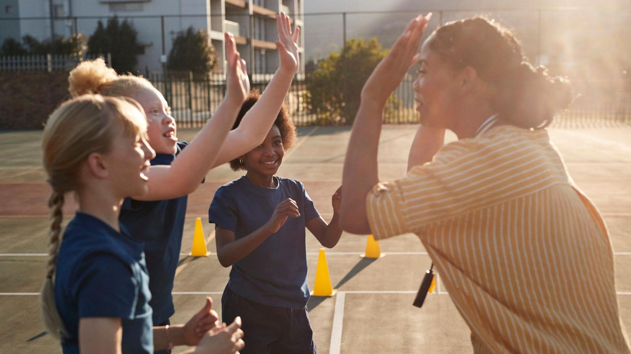 Three young pupils high five their teacher during a PE lesson.