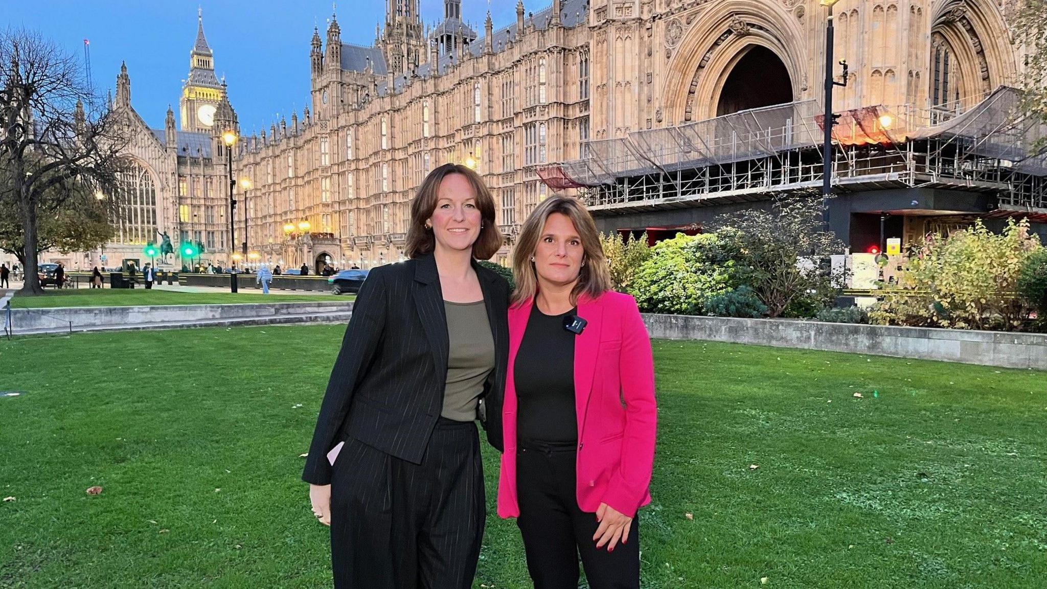 Lola McEvoy MP (left) and Ellen Roome (right) standing on the grass green with a backdrop of the Houses of Parliament 