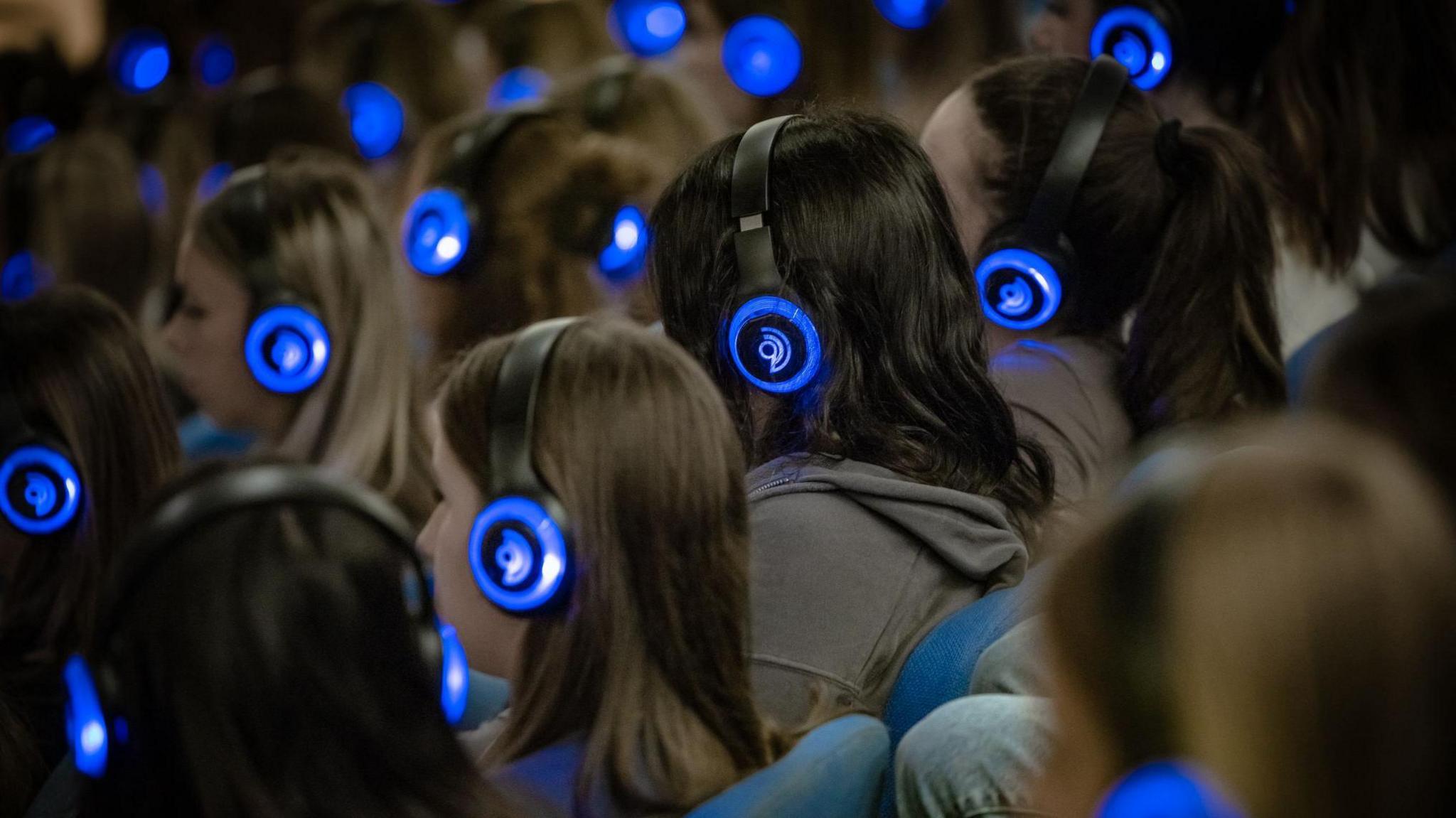 Children sitting in an auditorium with headphones, taking part in the breathwork technique.
