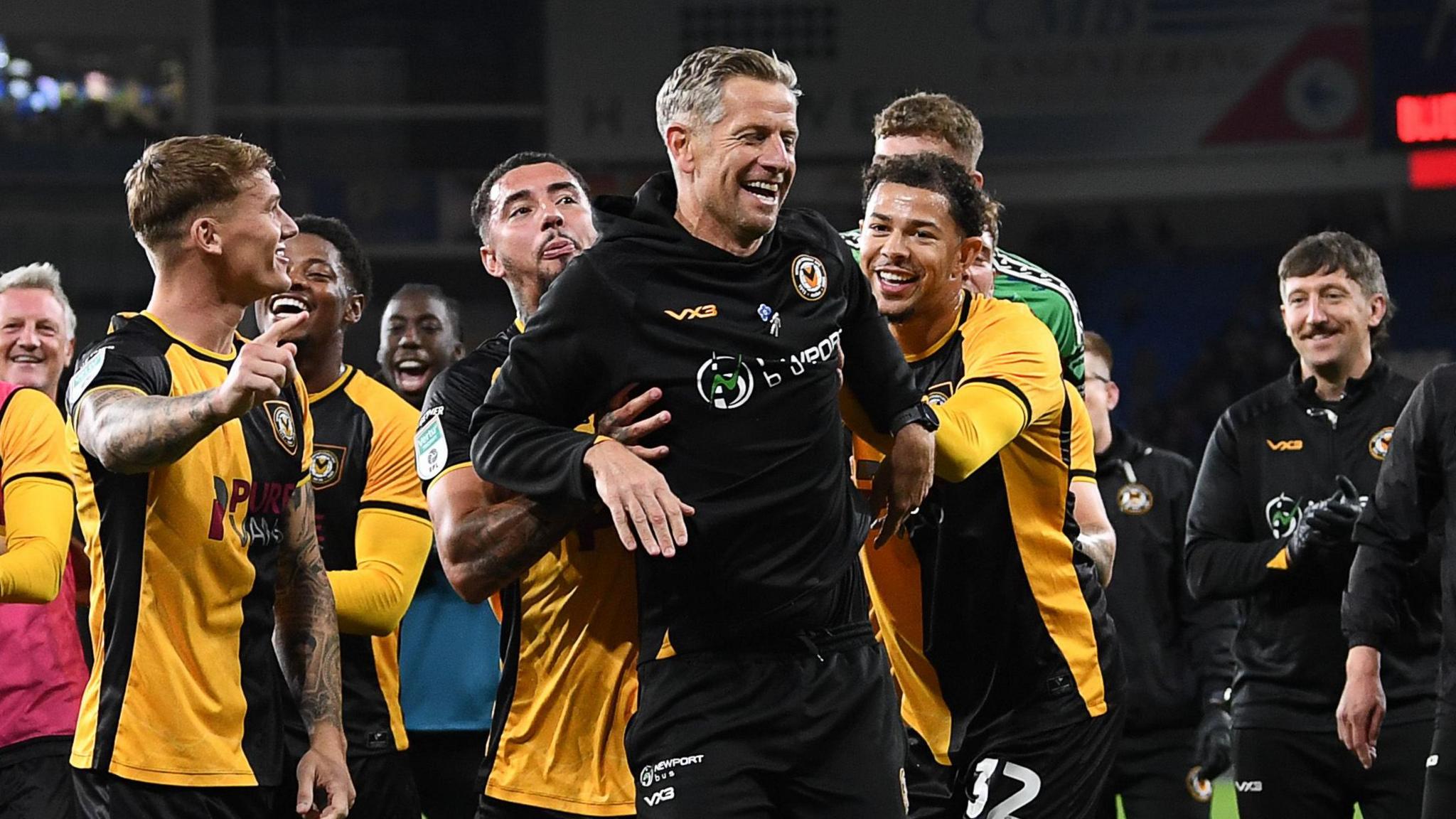 Newport players push David Hughes forward to celebrate their win at Cardiff with the away fans 