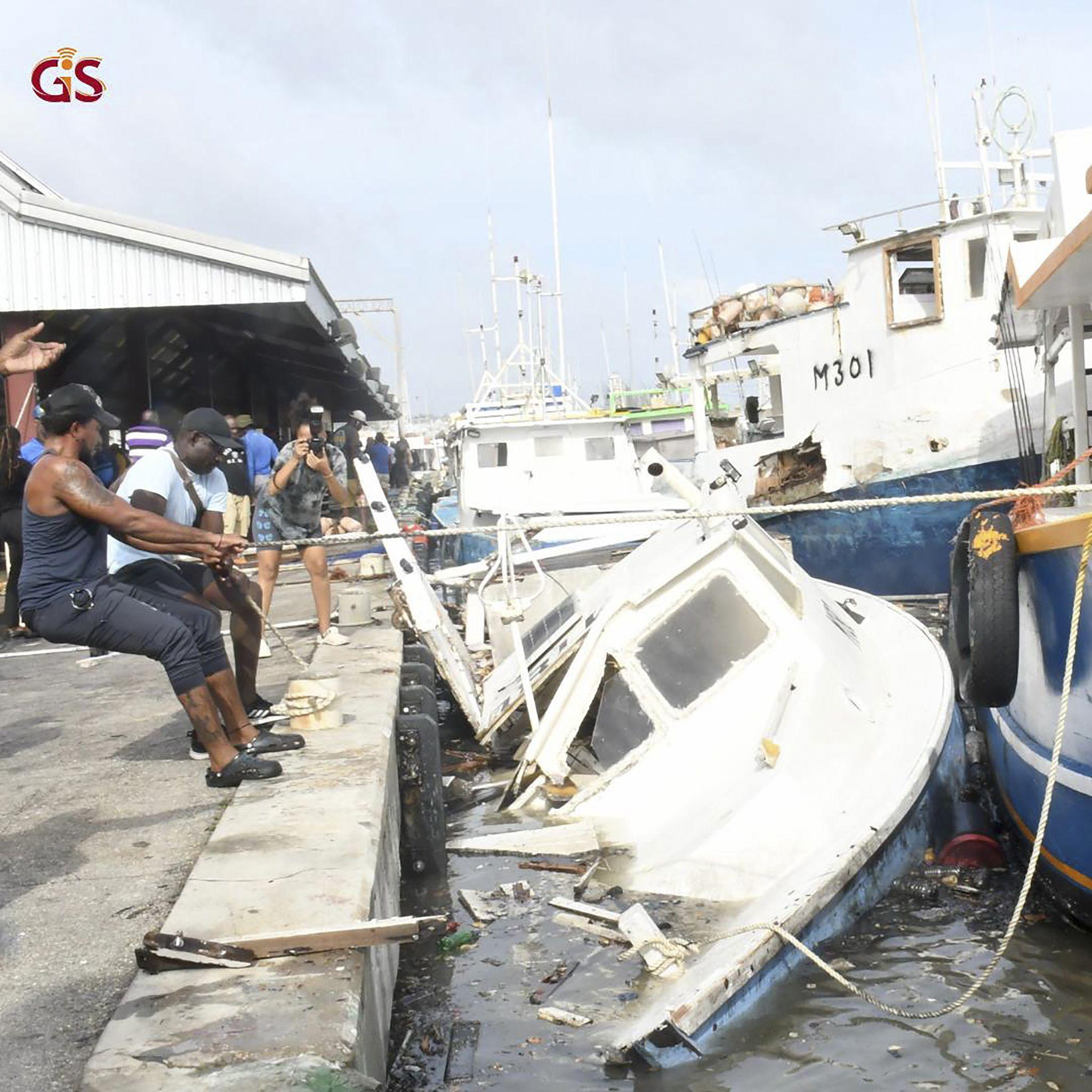 Men pull on a rope attached to damaged boats which are piled on top of each other at the harbour