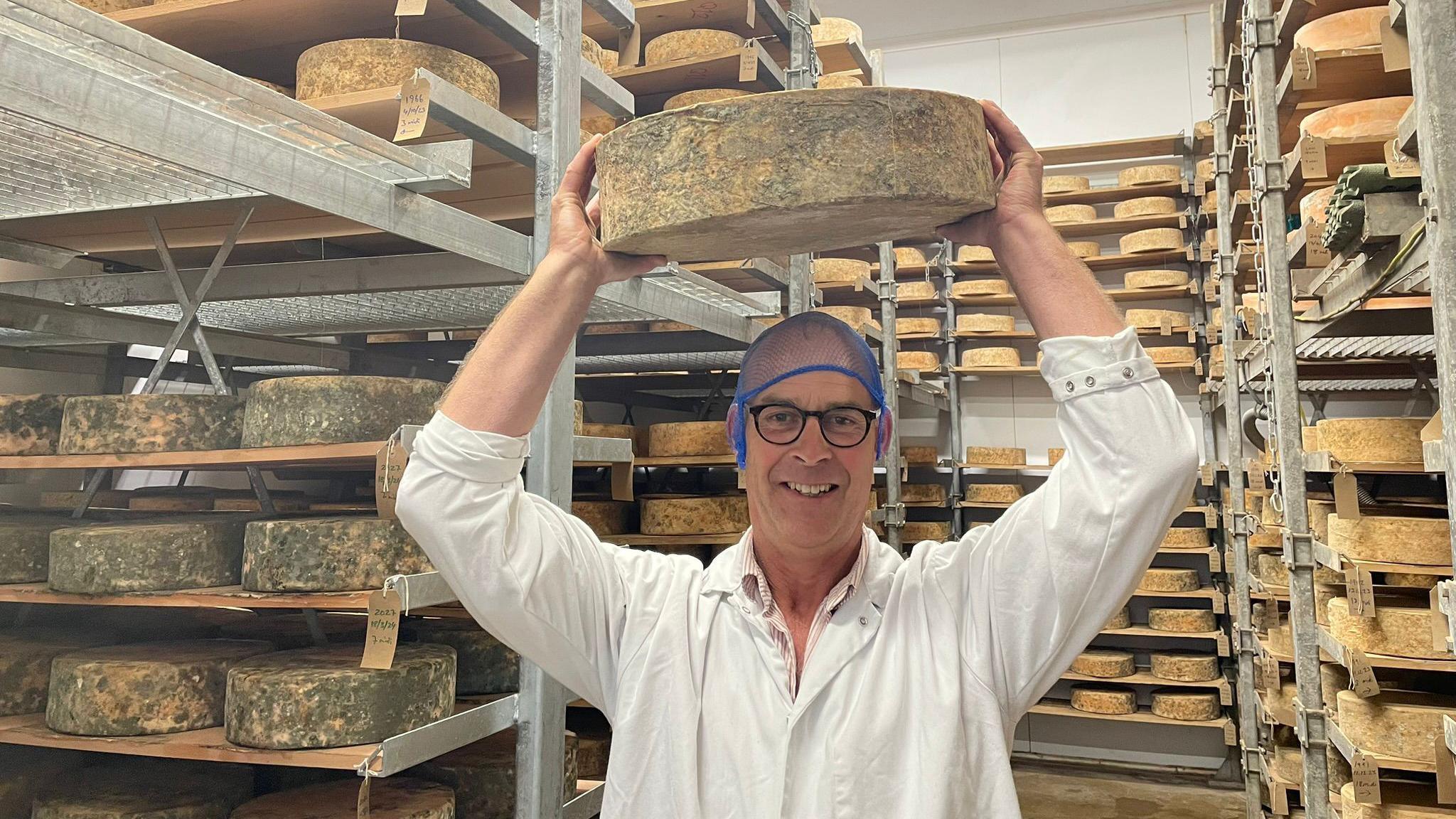 David Clarke in his cheese 'cave' holding up one of his Red Leicester cheeses 