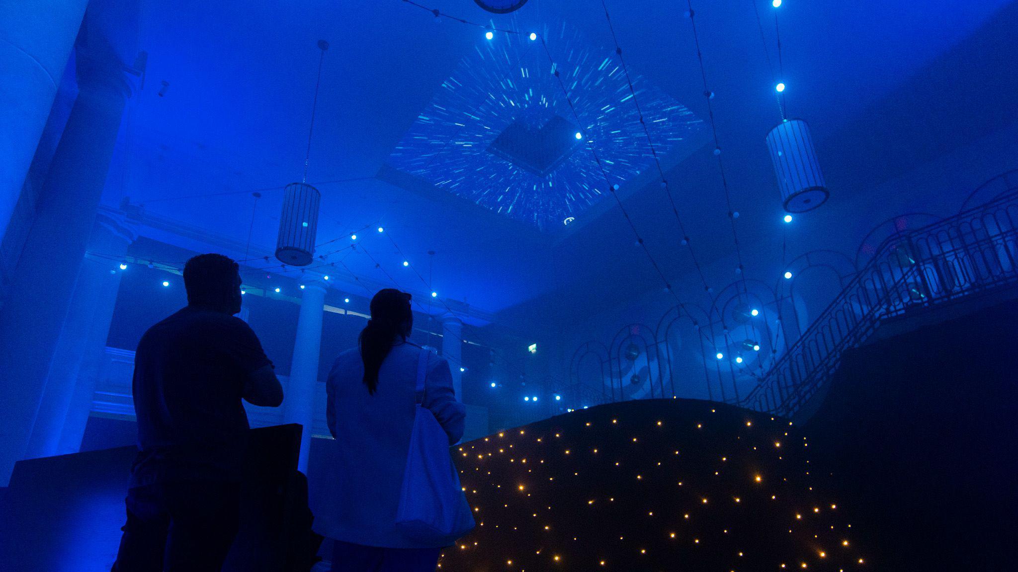 A man and a woman stand under bright pinpoints of light in dark room at the Lumosphere attraction in Cabot Circus in Bristol