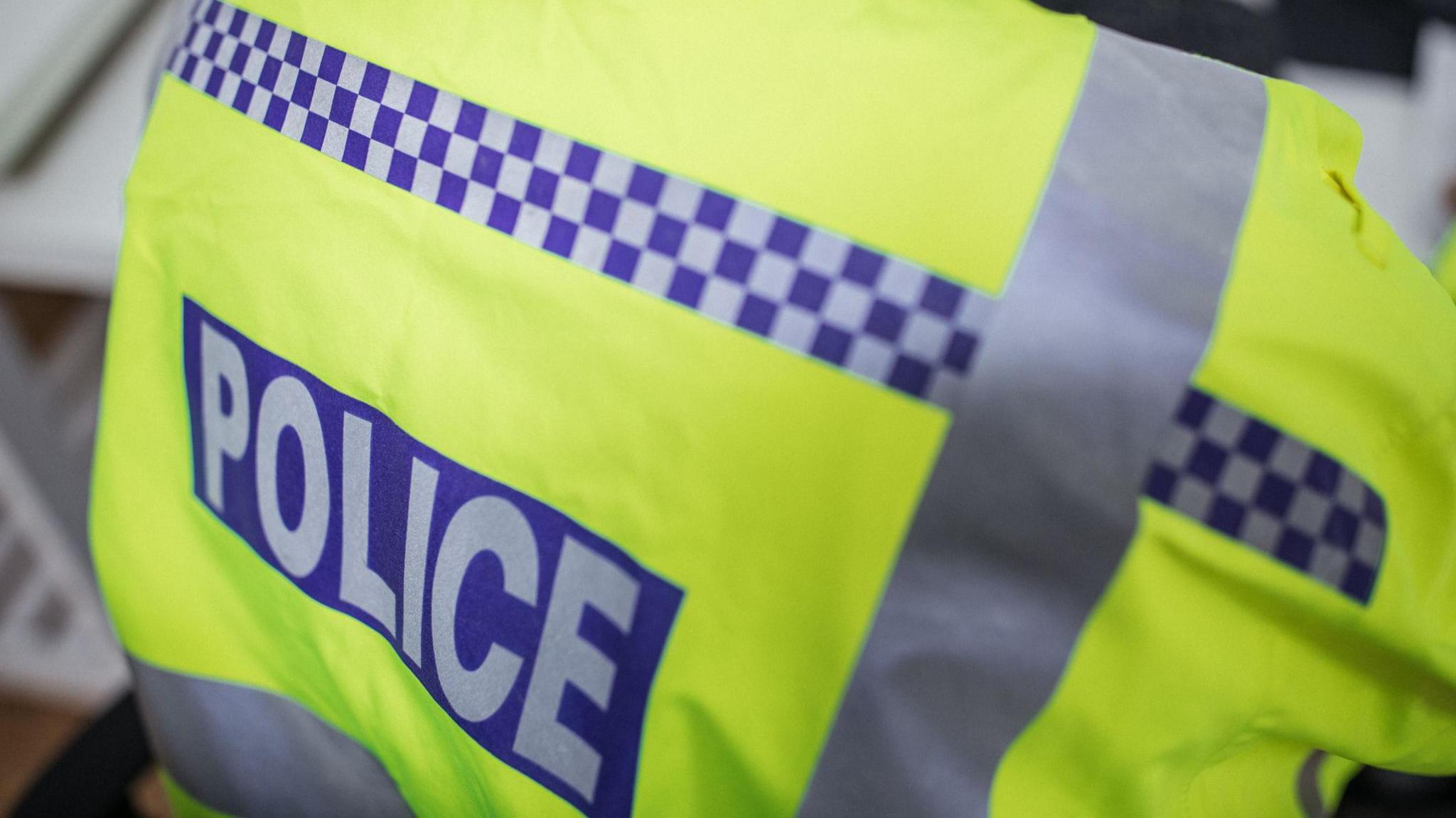 A close-up of the back of a police officer's high-visibility jacket. It reads 'Police' on it.