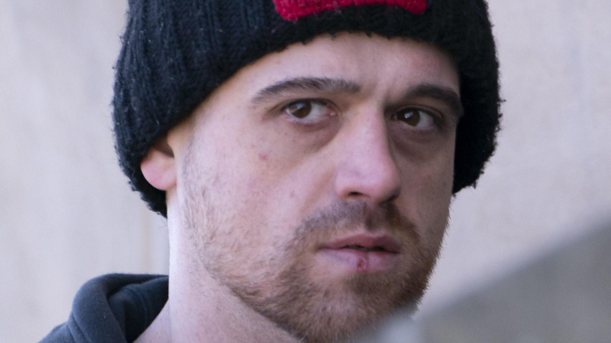 Richard Haslam, who has light brown stubble and is wearing a blue woolly hat with a Norway flag on the front, looks at the camera with a serious expression.