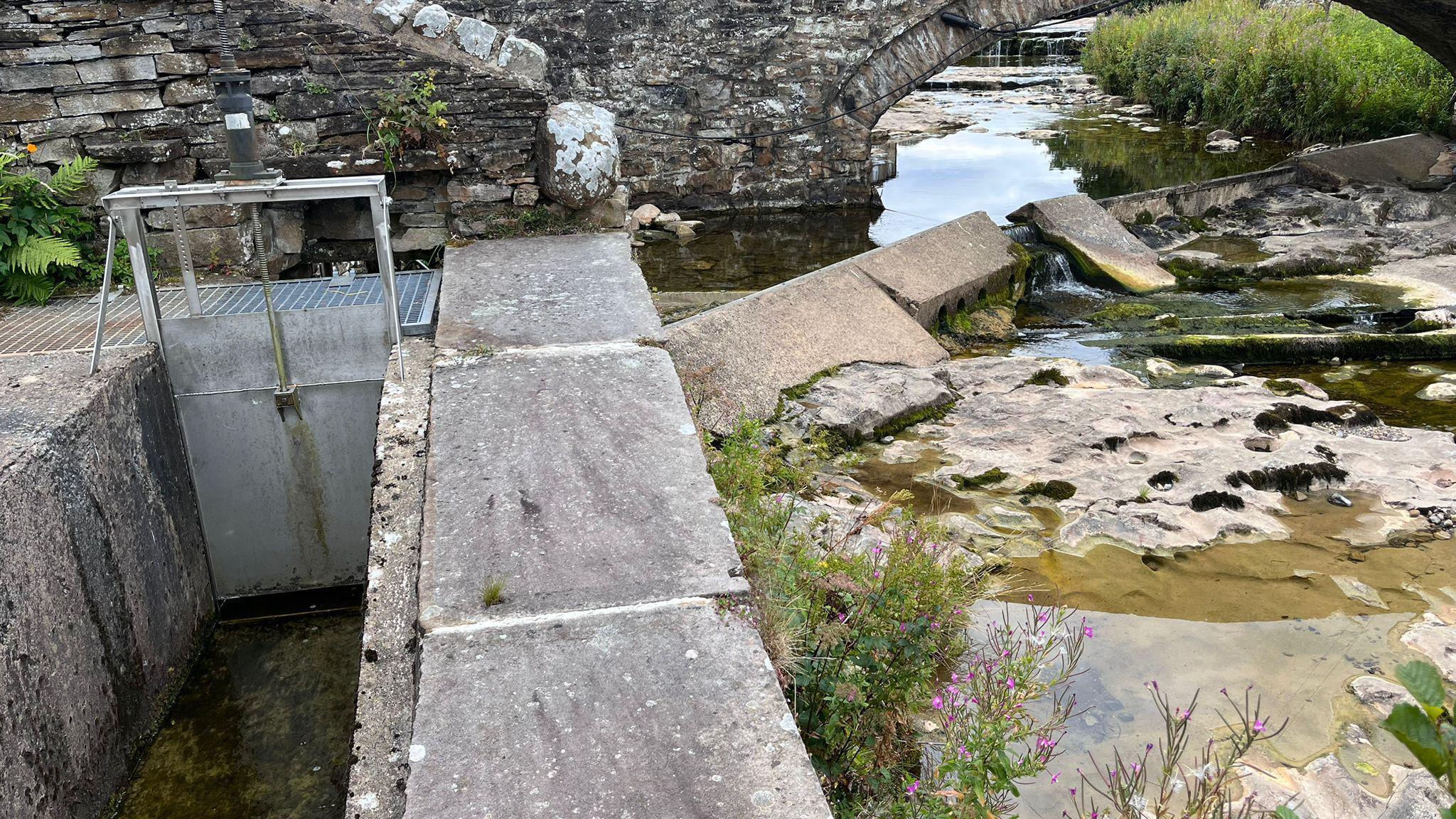 A mostly-empty passage which should be full of water, next to a Beck with stones at the bottom exposed, under water which would normally be gushing.