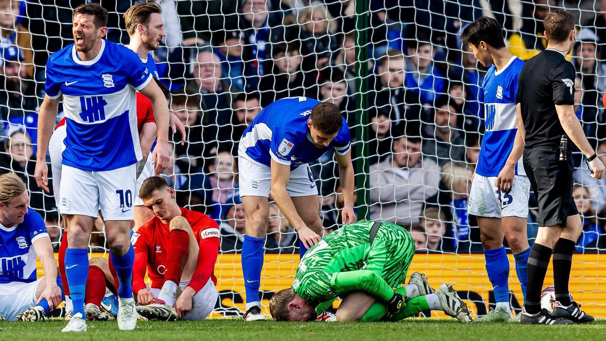 Ryan Allsop is kneeing with his face on the ground, holding his left leg after suffering an injury against Wycombe