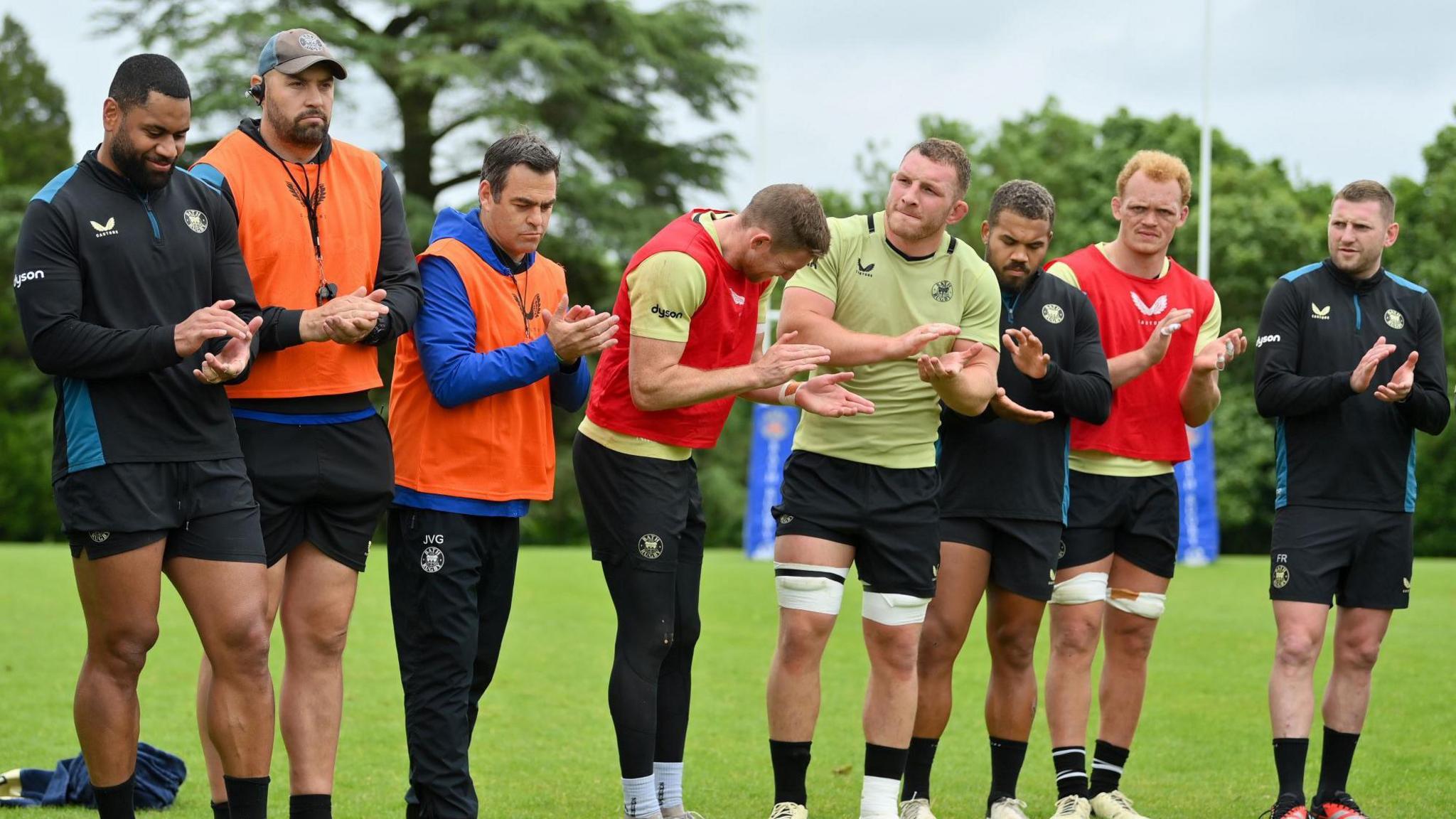 Bath players and coaches stand in a line during training