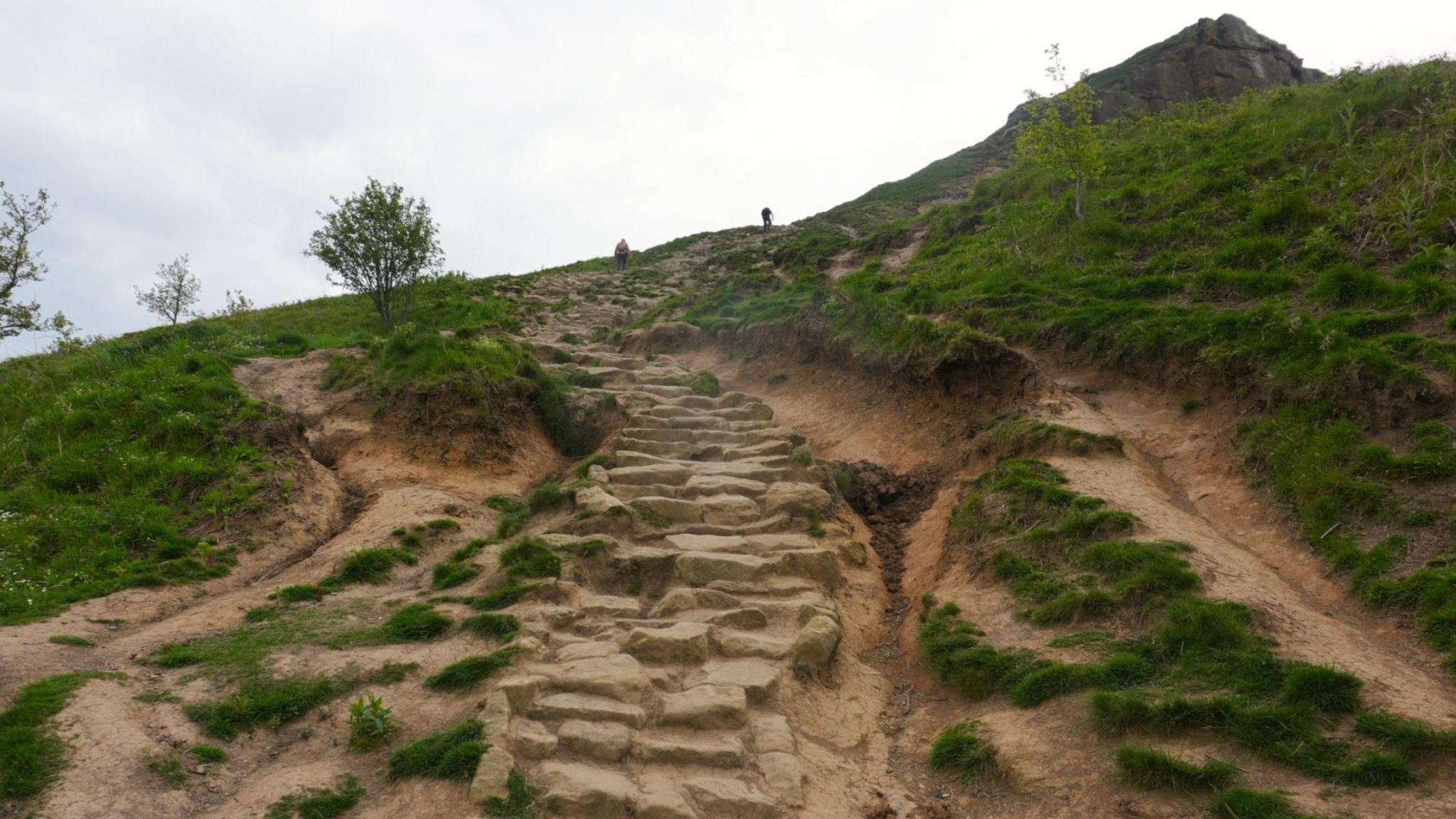 Stone steps leading up the hill where the ground is eroded on either side, creating dips.