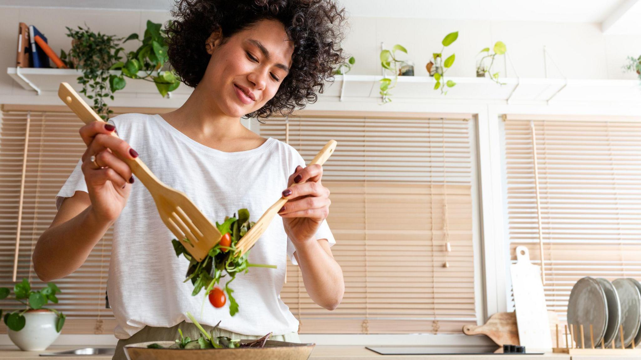 Happy young woman mixing bowl of fresh salad.