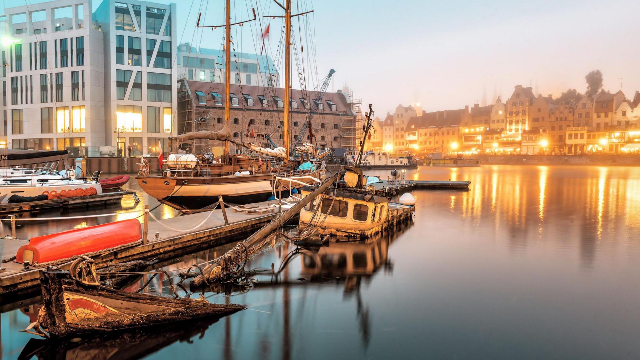 A sunken boat in Gdansk harbour with other boats around it and houses and buildings in the background