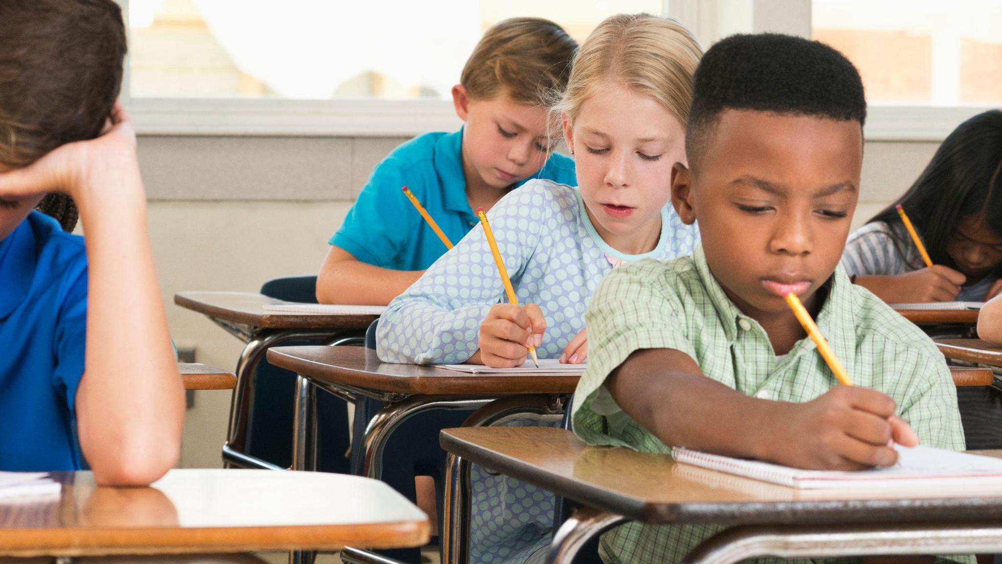 primary school pupils sitting at desks with yellow pencils taking a test