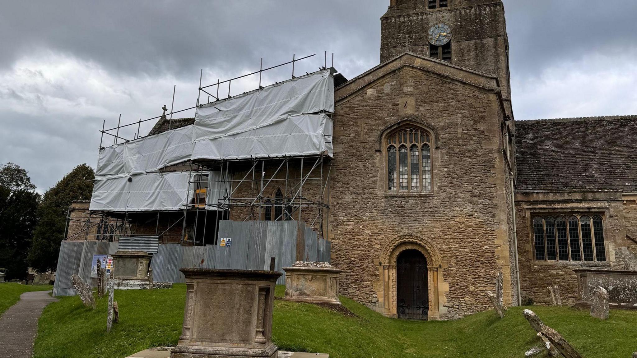 The front of st mary's church, with one portion covered by scaffolding and white covering. In front of the church is a garveyard.