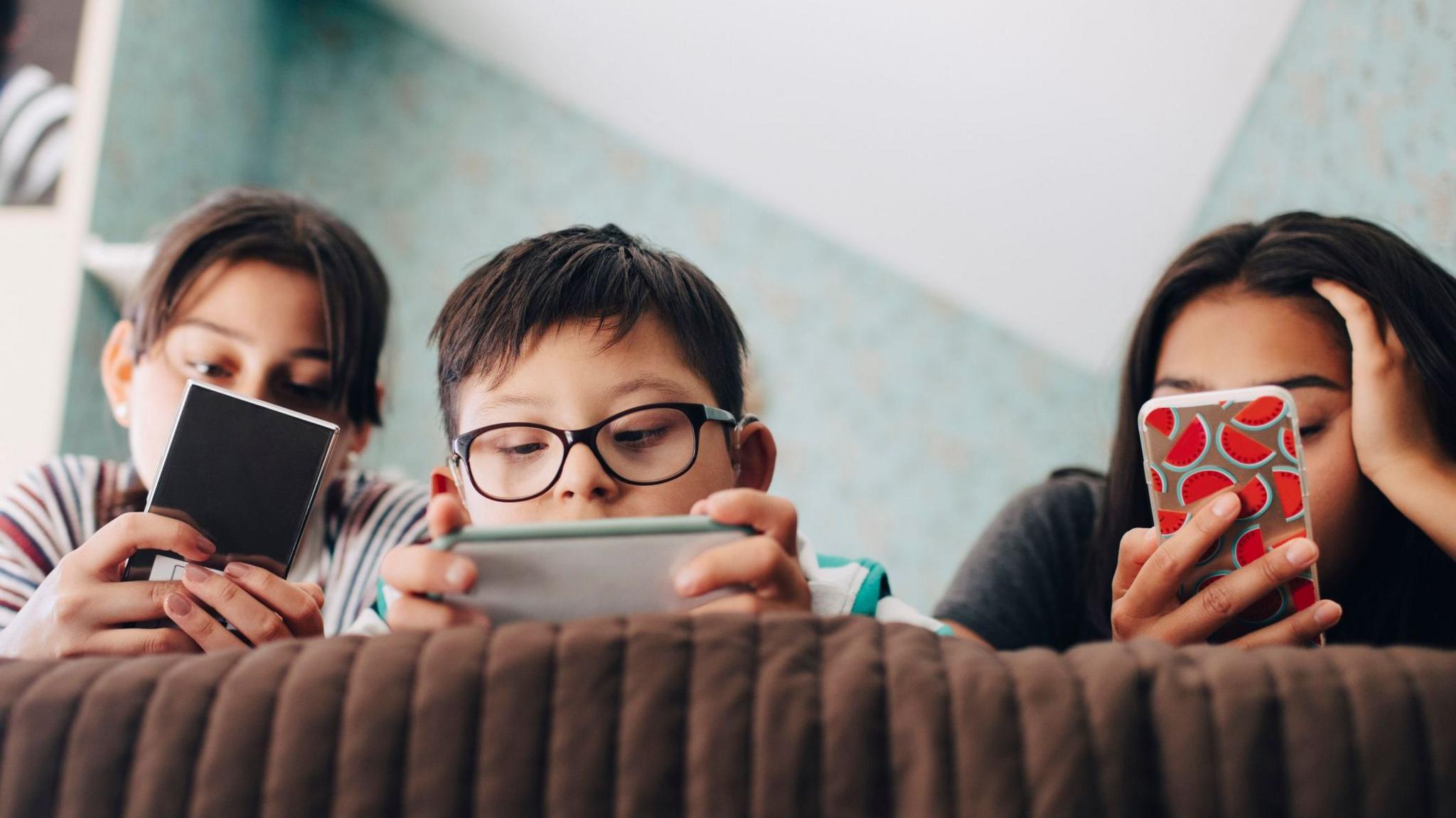 Three children staring at phones they are holding.