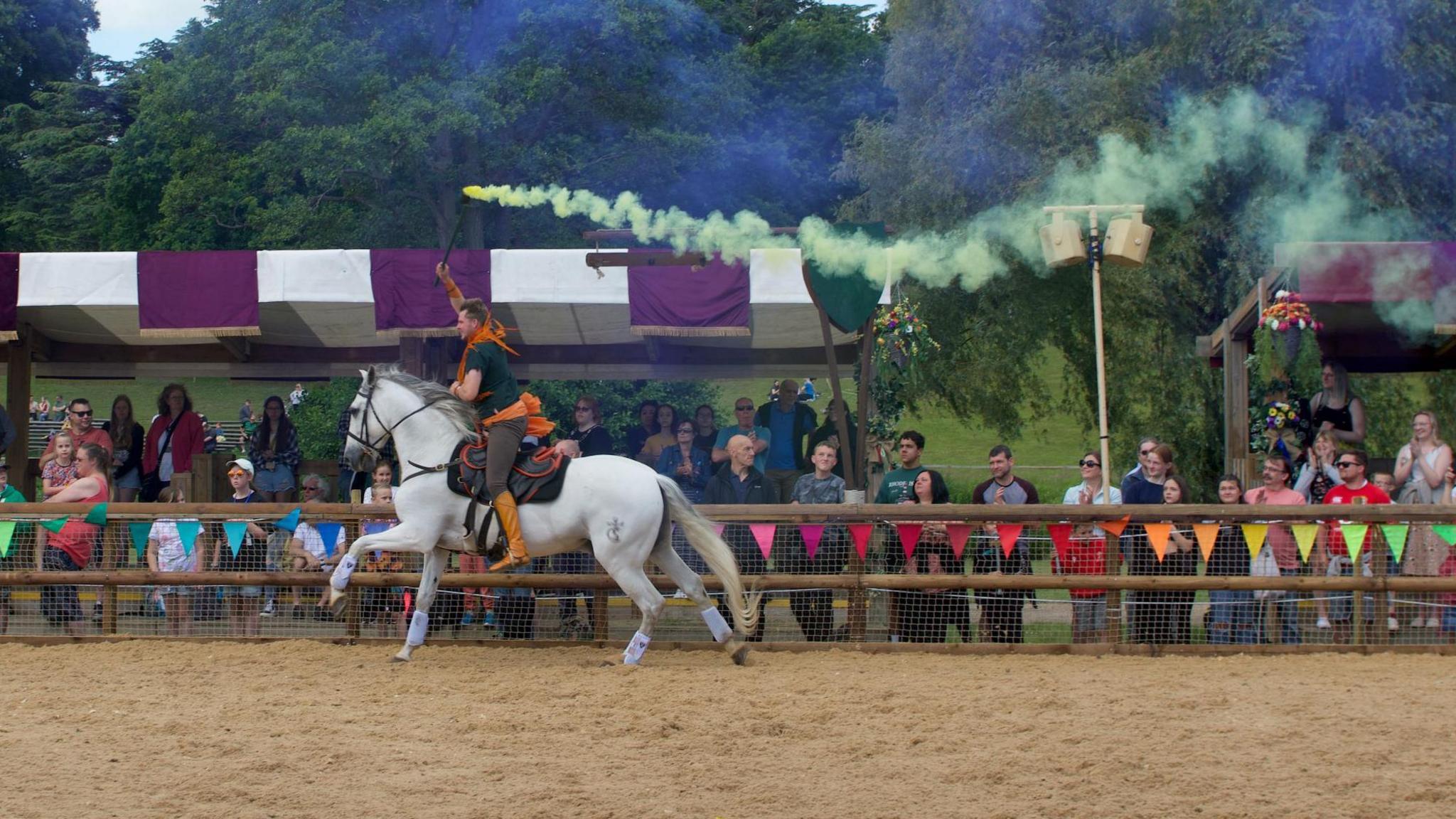 A man riding a white horse holding a yellow flare above his head with crowds watching on