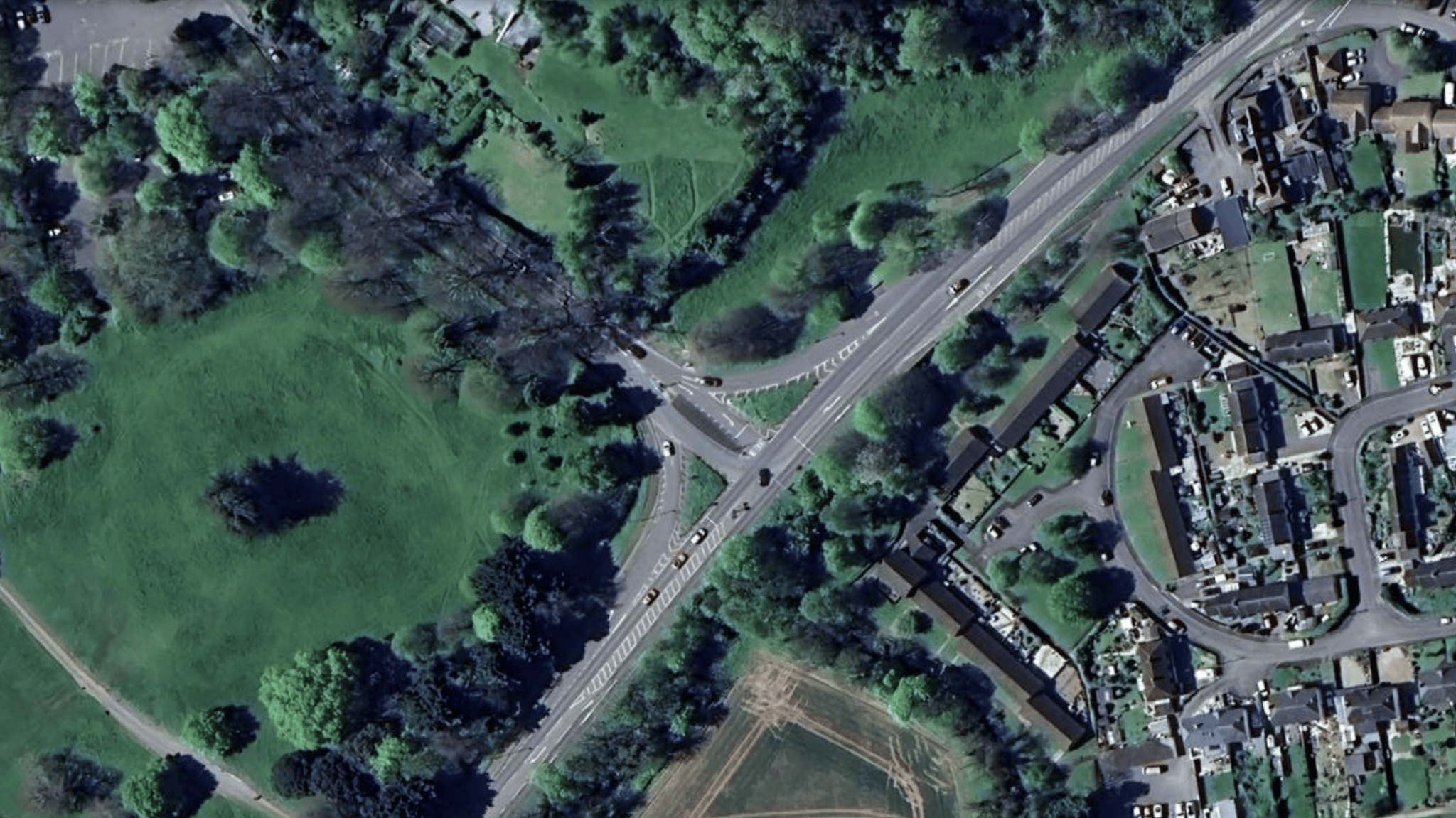 A birds eye view of the junction. To the left there is a green field and to the right there is a housing estate.