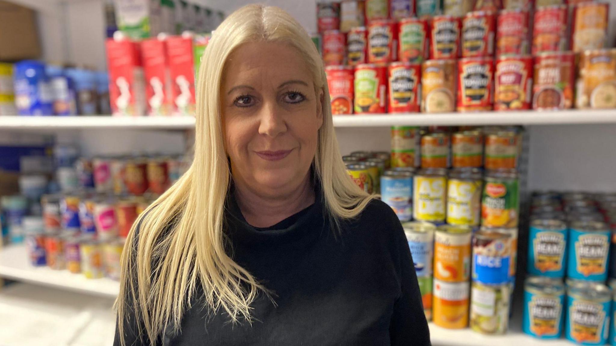 A blonde woman standing in front of shelves of tinned food