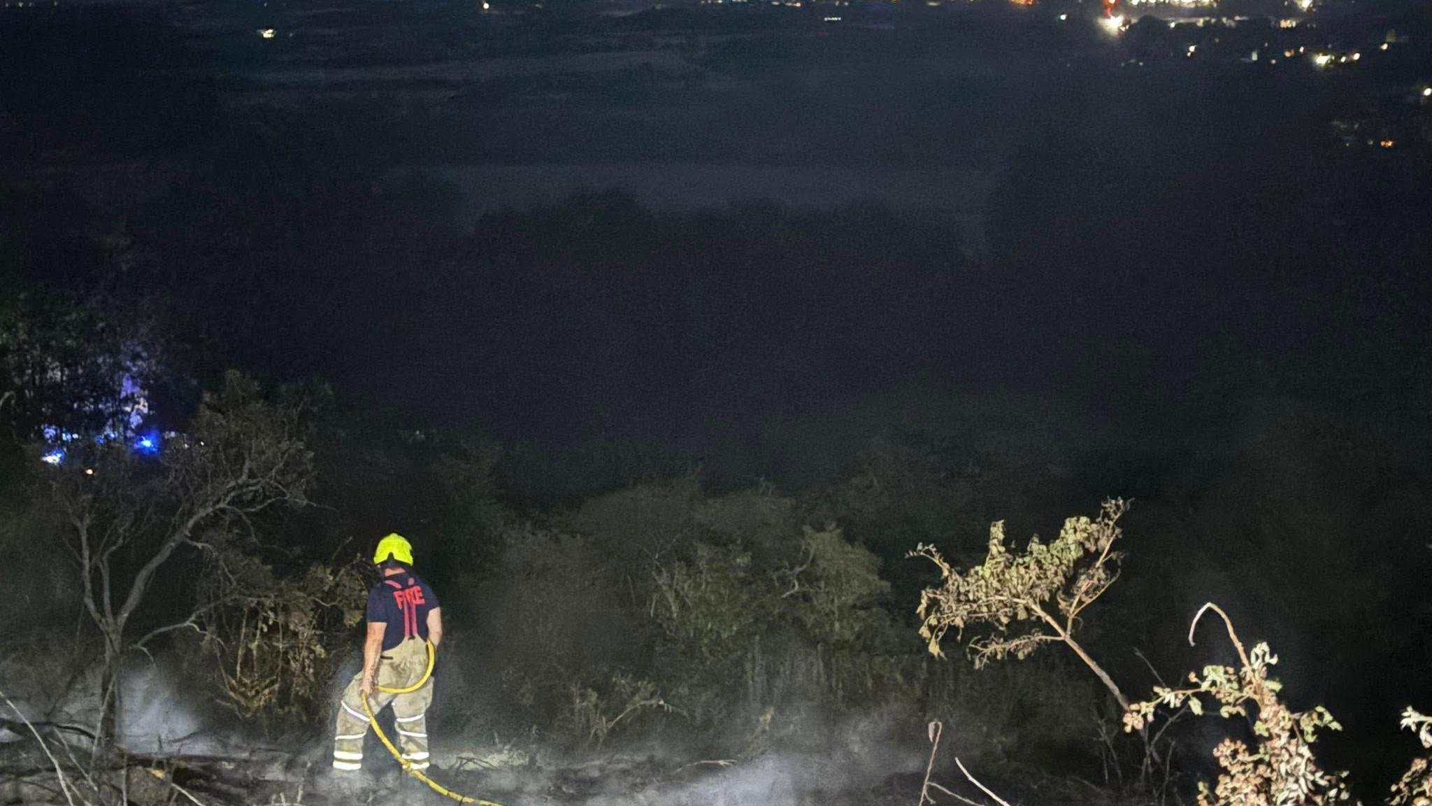 Firefighter standing in a burnt area of grassland at night after a large fire at Croft Hill, Leicestershire.