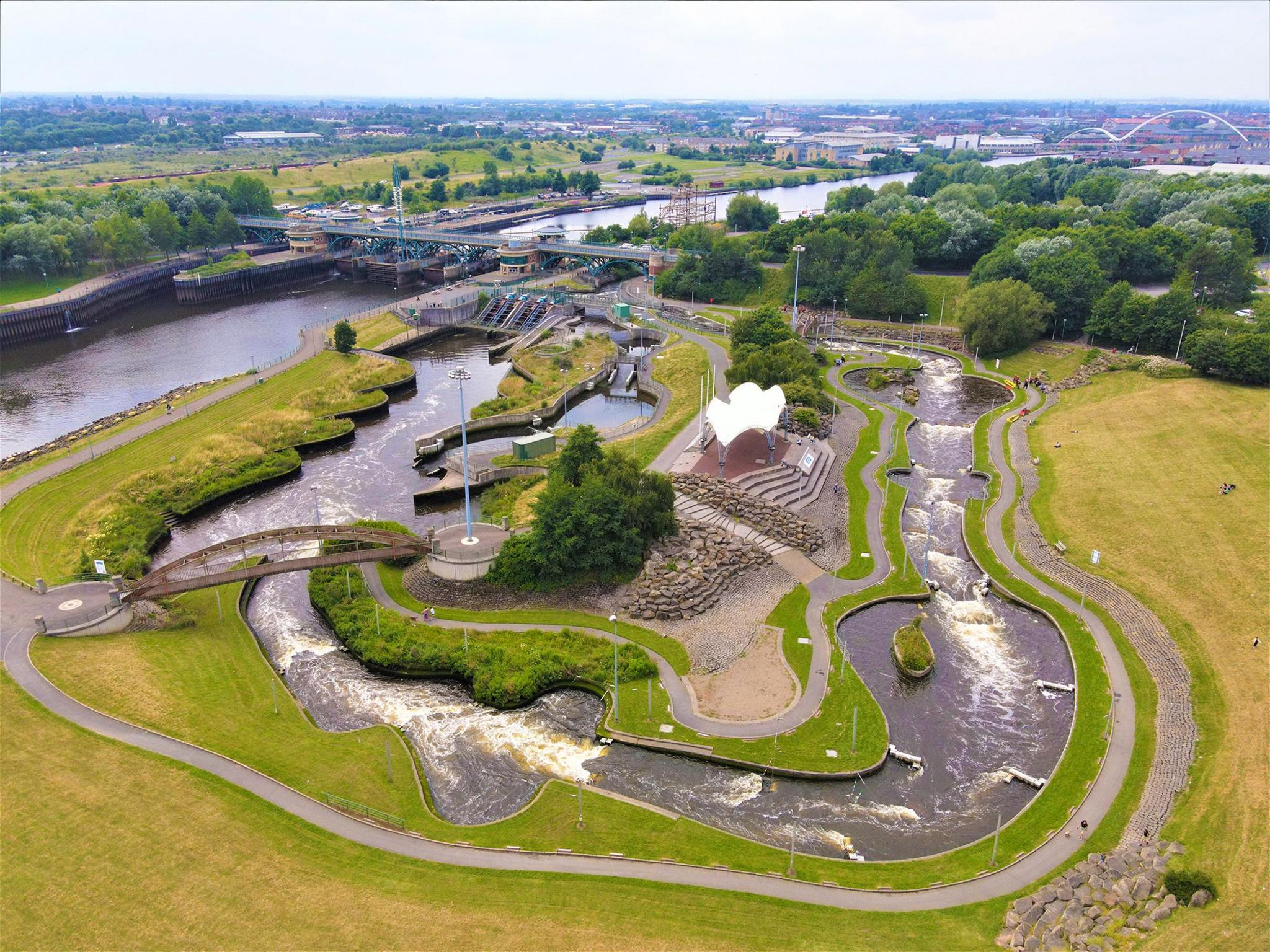 Aerial view of the water course. A water way snakes around the landscape with various bridges, pavements and shrubbery surrounding it.