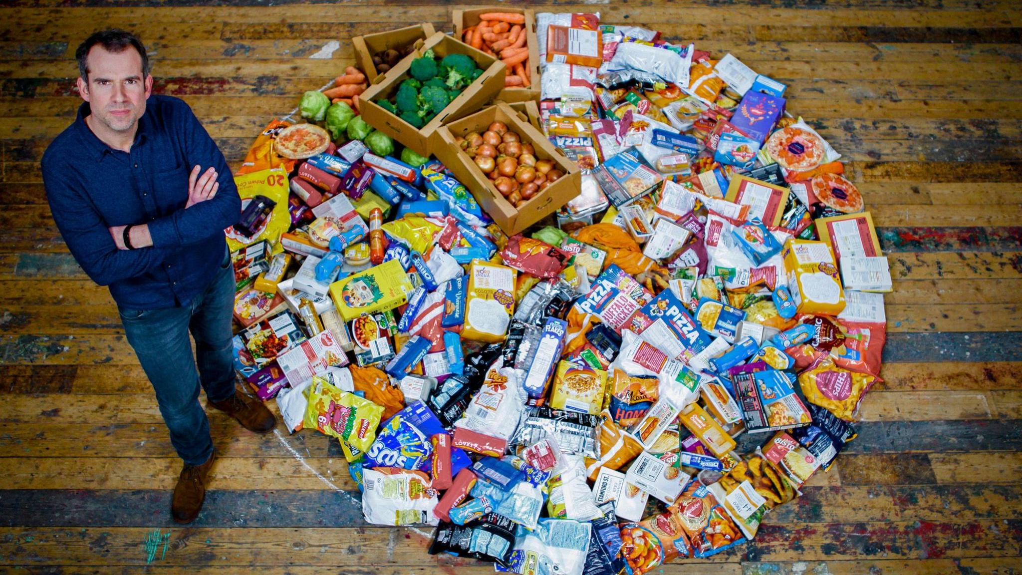 Dr Chris standing next to a pile of ultra processed food.