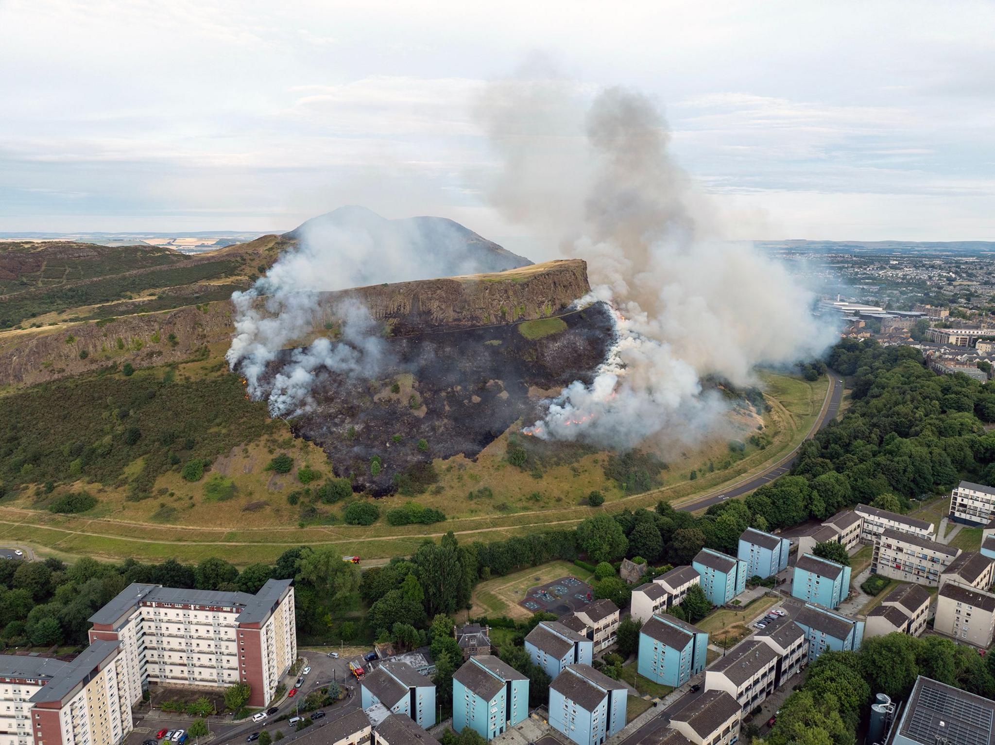 An aerial shot of white plumes of smoke coming from Arthur's Seat.