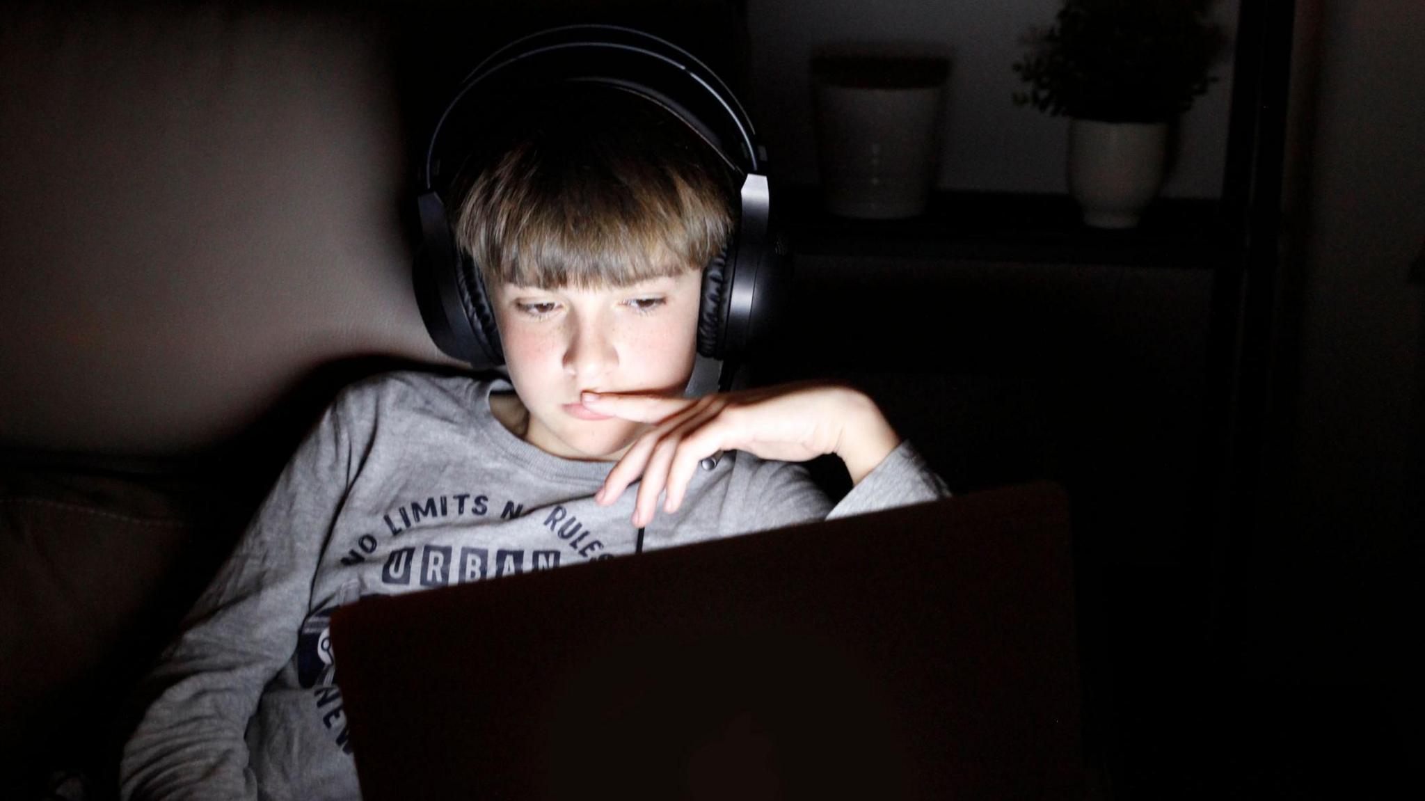 Boy using laptop on sofa at night wearing noise cancelling over-head headphones.