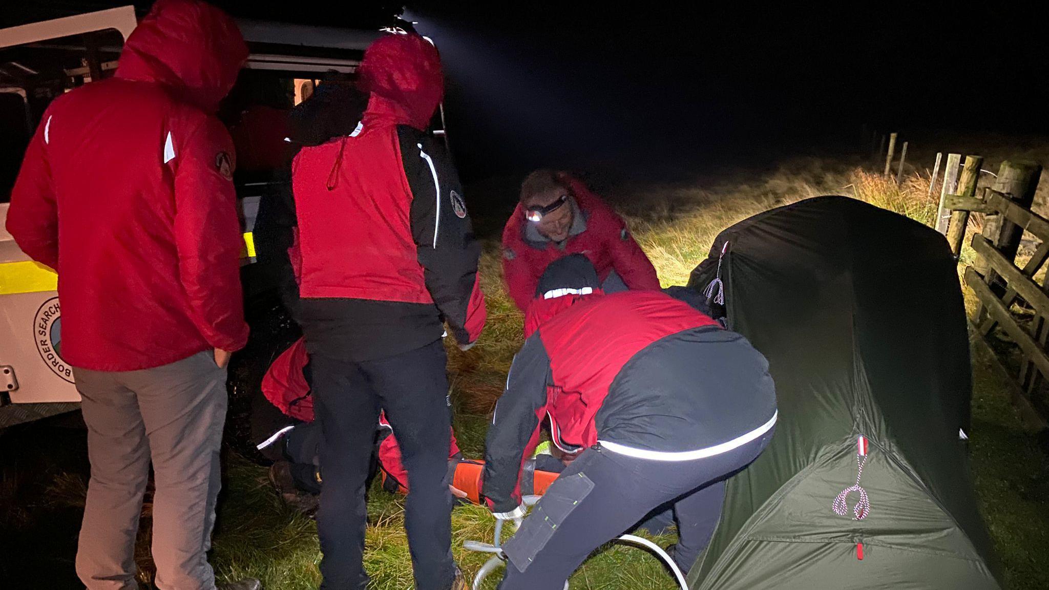 A rescue team with head torches on helps a man on a stretcher out of his tent on a Borders hillside