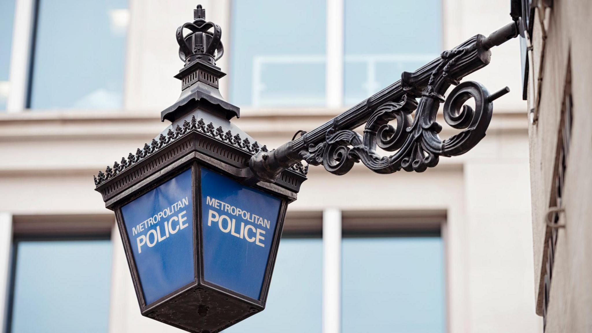 A lamppost which has the words metropolitan police on it in white letters and has a black handle with ornate metalwork on it