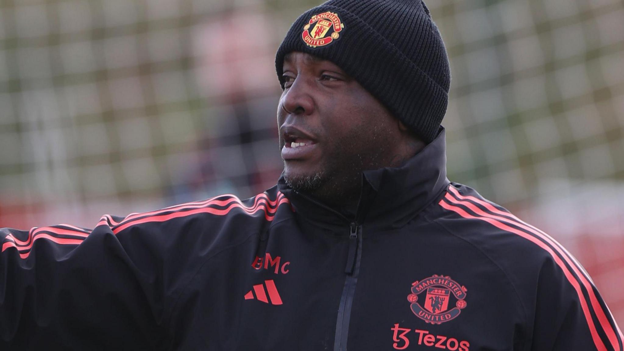 Benni McCarthy wears a branded black bobble hat and black tracksuit top with red trim during a training session with Manchester United