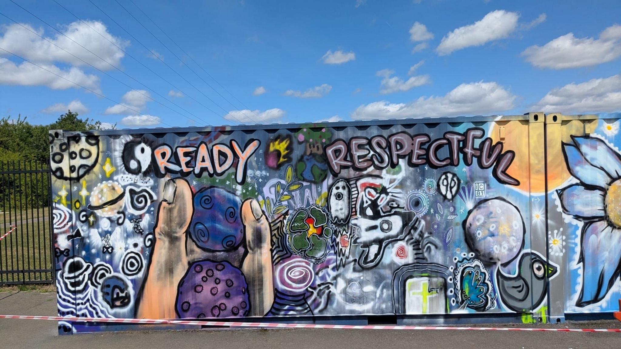 A mural which has different images, including a finger and thumb holding two purple rocks, a space ship and space scene, a bird and a large flower which has  yellow centre and white flowers. 