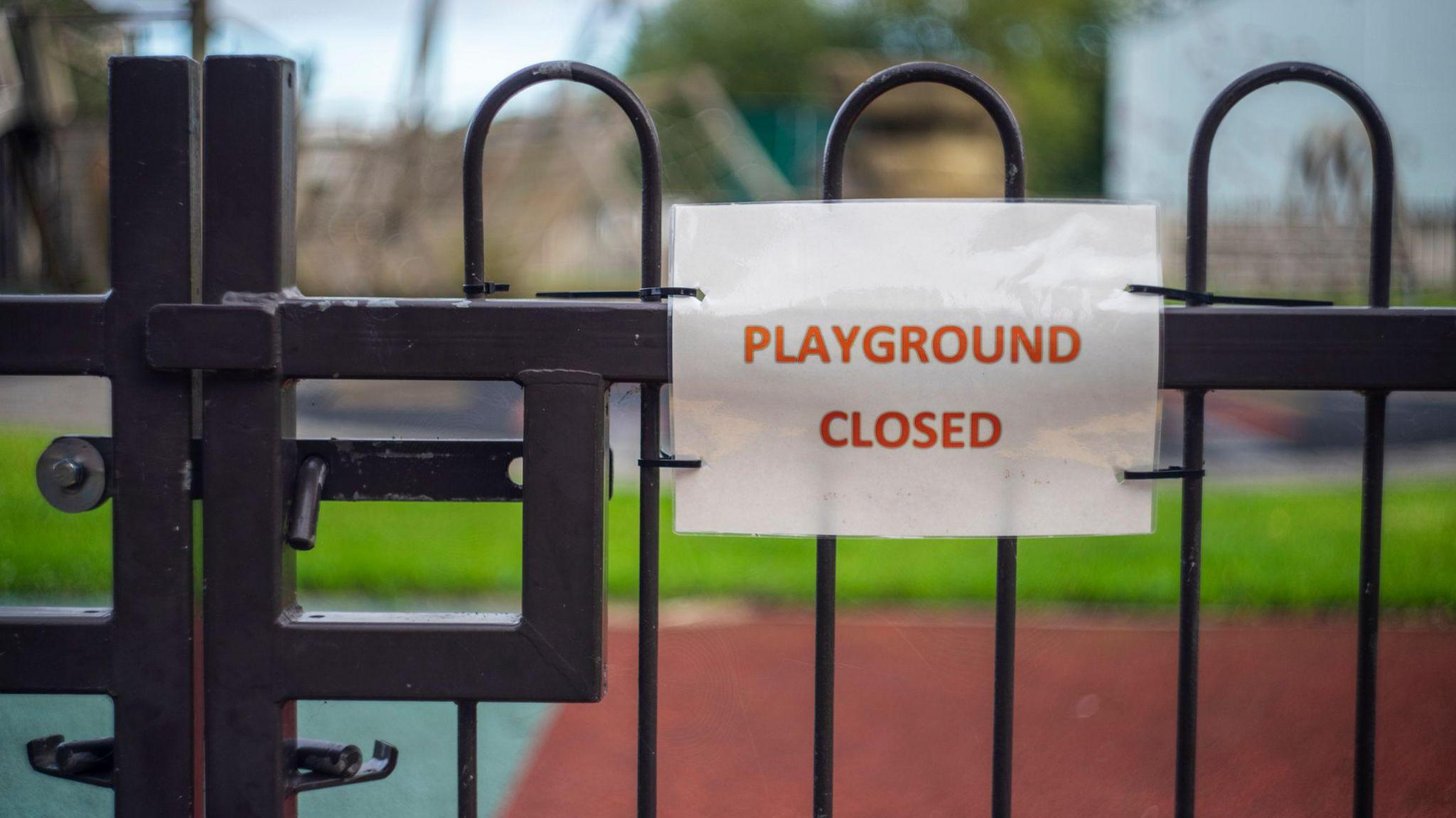 A playground gate with a sign attached which says "PLAYGROUND CLOSED"