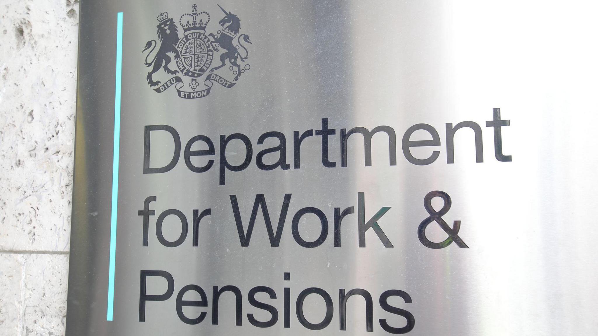Close-up of a grey metal sign which says "Department for Work and Pensions". The government's logo containing a unicorn and a lion is above it in the top left corner.